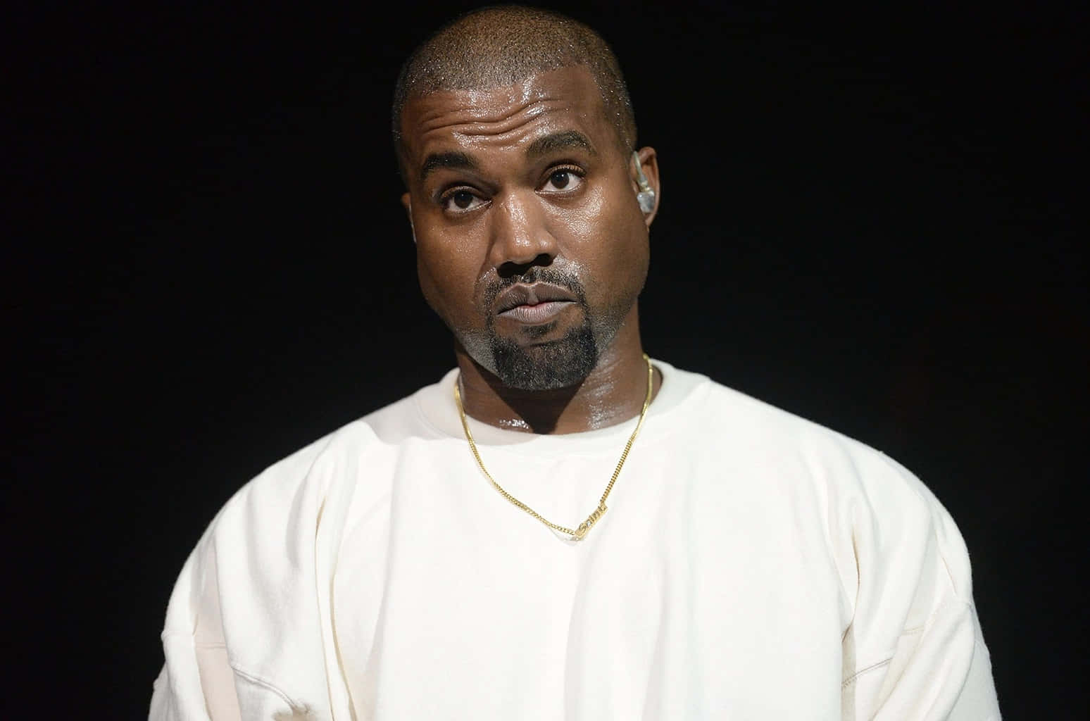 Kanye 桌布 壁紙 — Kanye West 在黑色背景前，穿著一件純白色衛衣，戴著一條金鍊，專注地凝視。