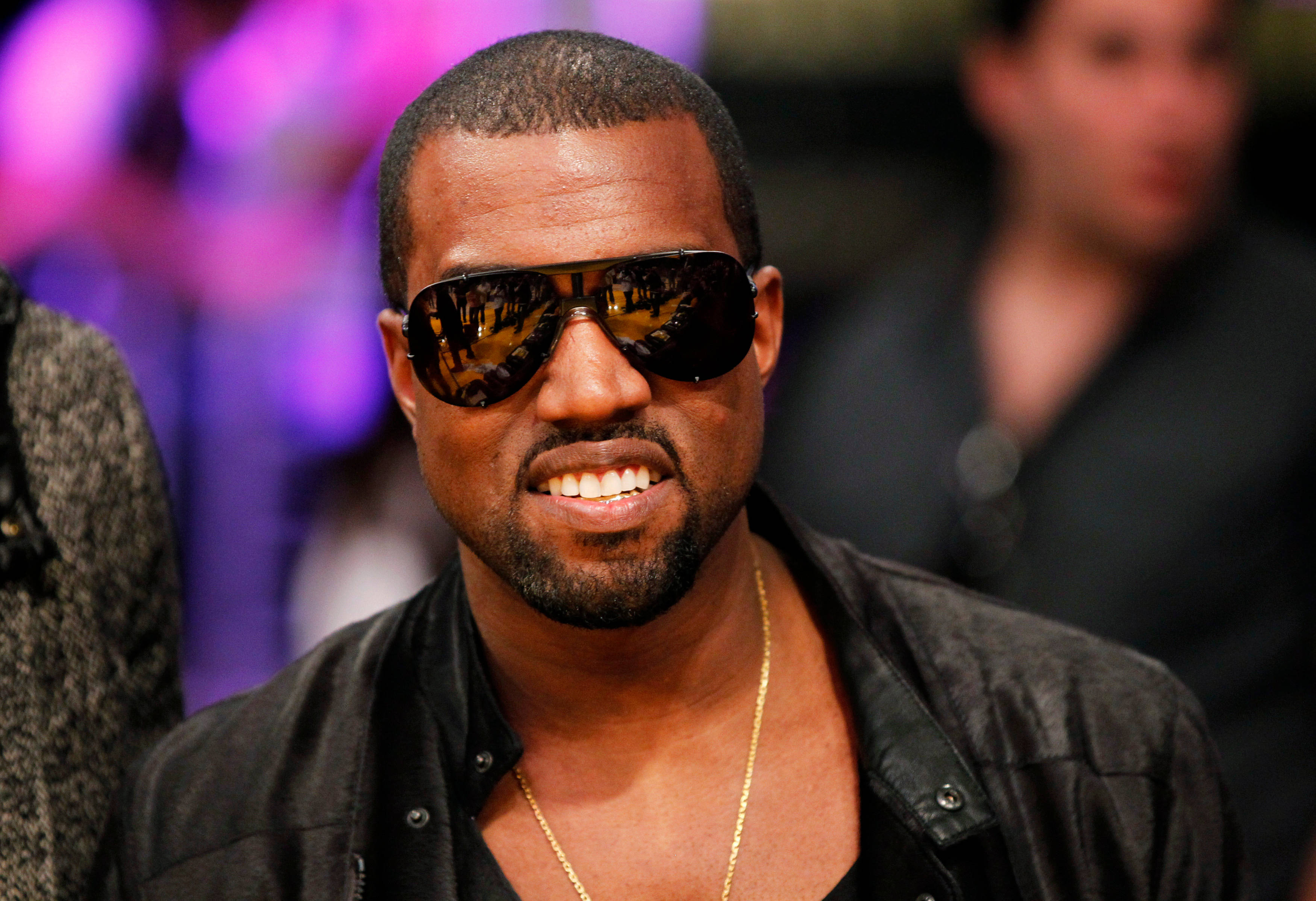 Kanye 桌布 壁紙 — Kanye West 自信地微笑，戴著深色太陽眼鏡和黑色外套，背景是模糊的紫色。
