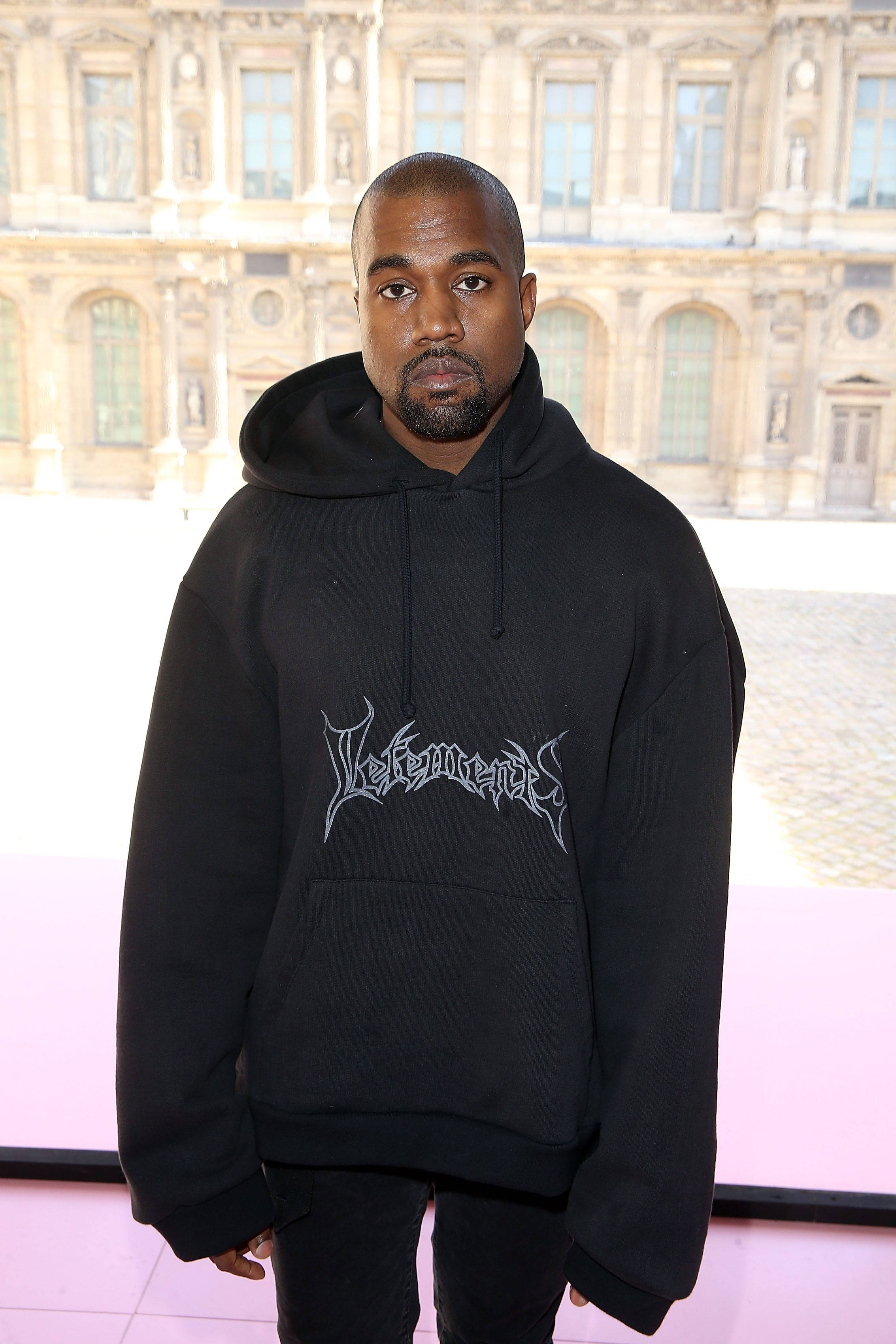 Vetements 桌布 壁紙 — Kanye West 身穿印有 'Vetements' 標誌的黑色連帽衫，站在宏偉的石砌建築外牆前。