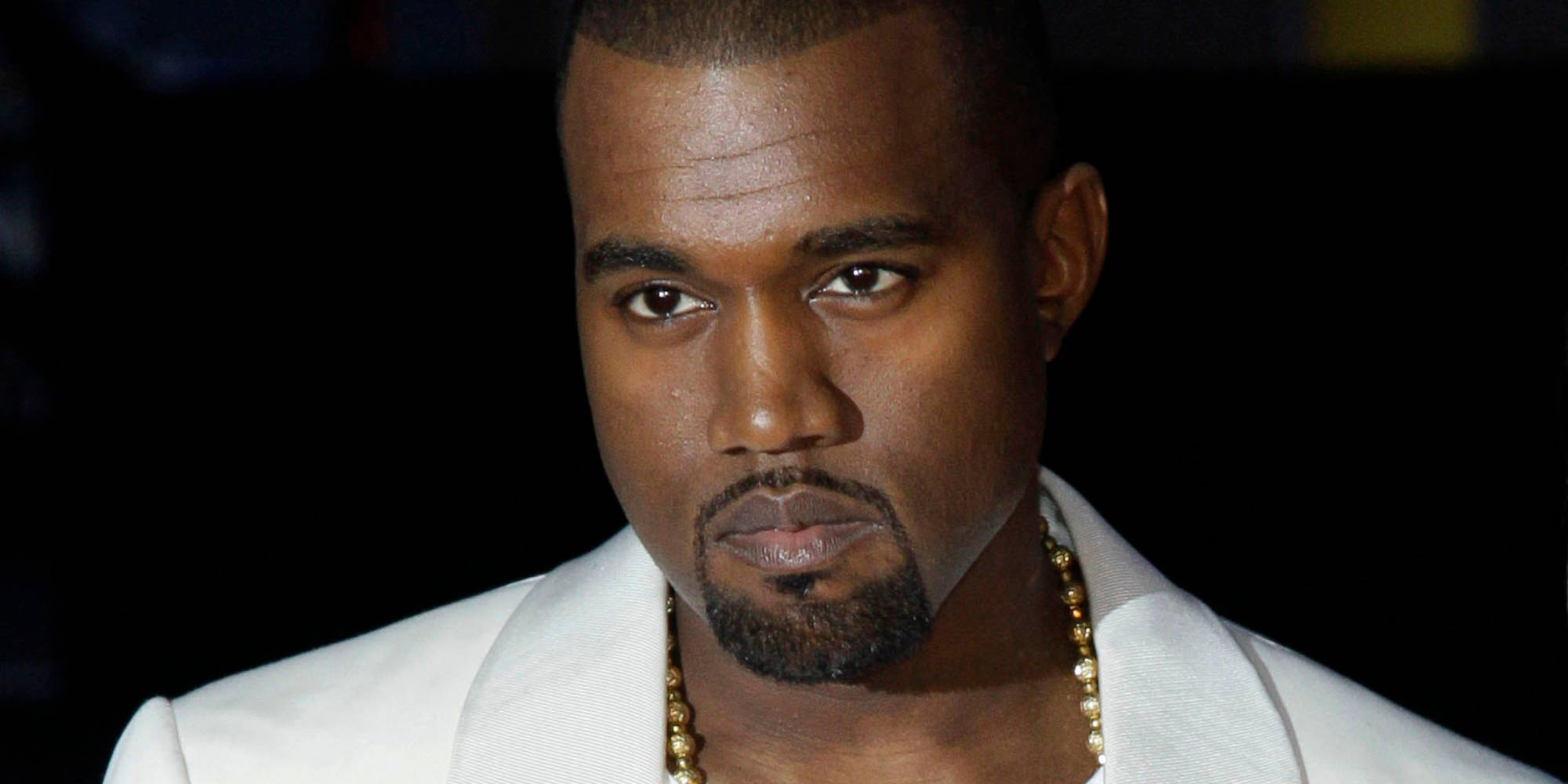 Kanye 桌布 壁紙 — Kanye West 身穿白色西裝和金色鏈條，在深色背景下的特寫肖像。