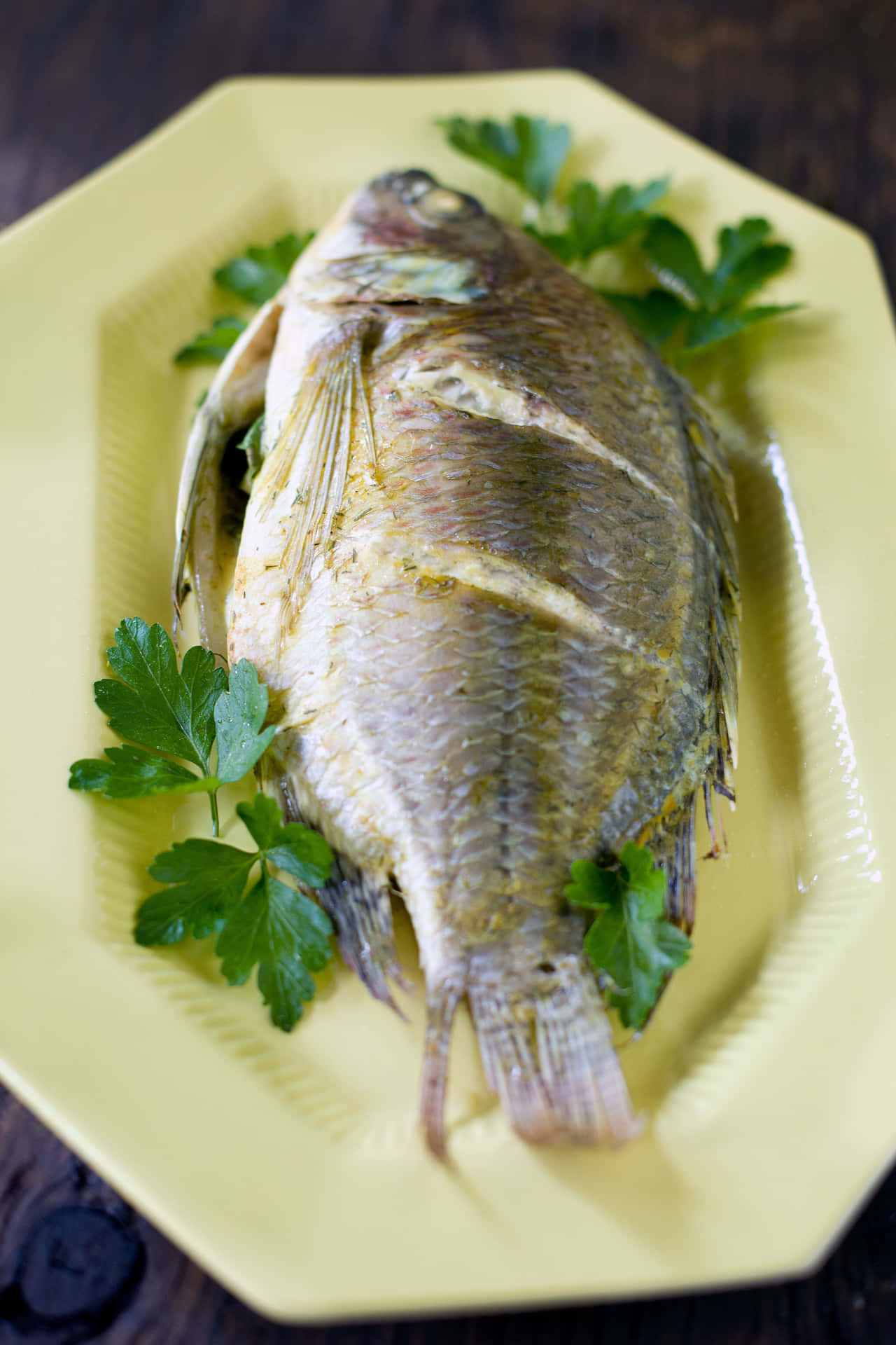  壁紙 — 一條烤全魚，魚皮酥脆，配上新鮮歐芹，放在淺黃色盤子上，置於深色木桌上。