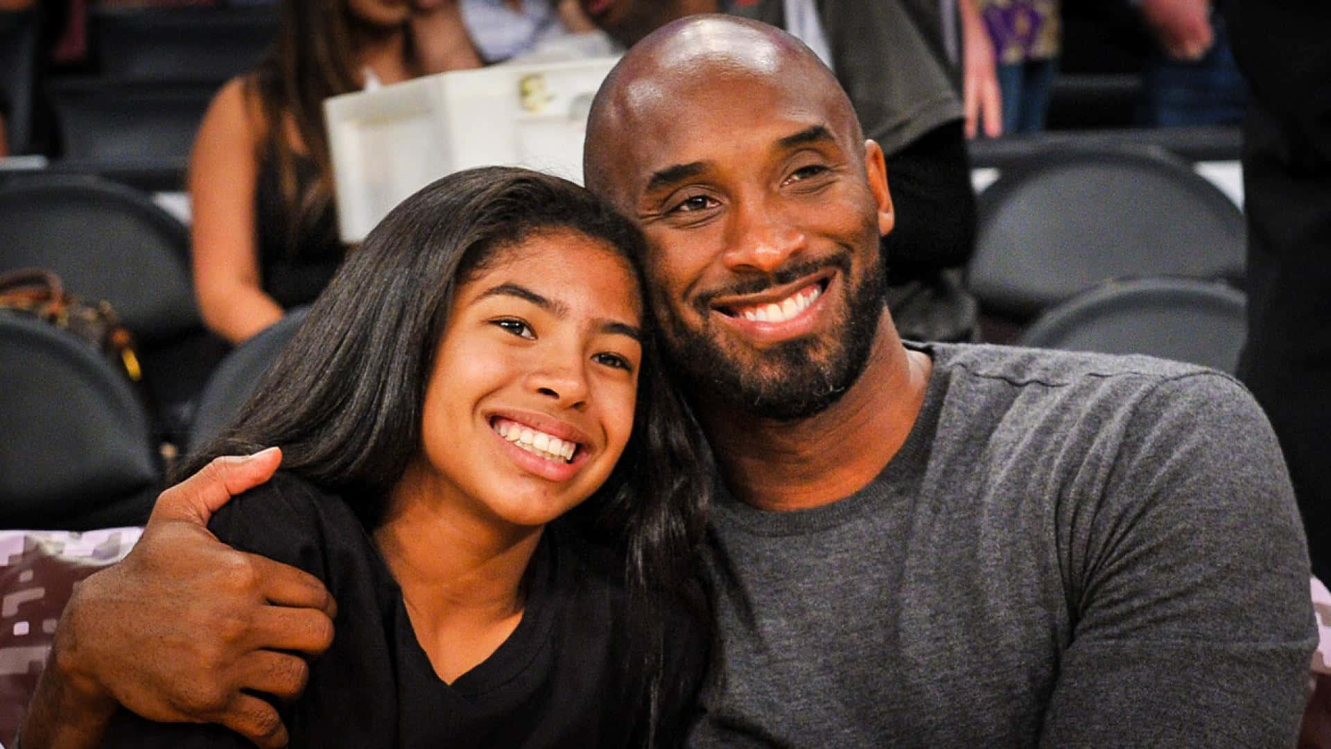 Kobe And Gigi 桌布 壁紙 — 柯比布萊恩與女兒吉安娜在籃球場的座位上溫暖地微笑。