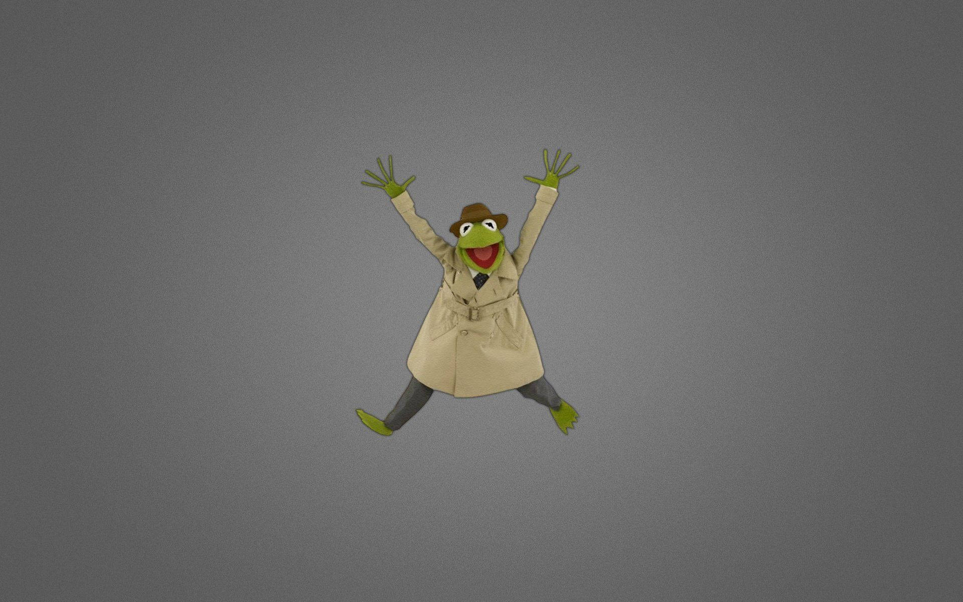 kermit 桌布 壁紙 — Kermit the Frog 穿著米色風衣和軟呢帽，在純灰色背景上舉起雙臂歡快地跳躍。