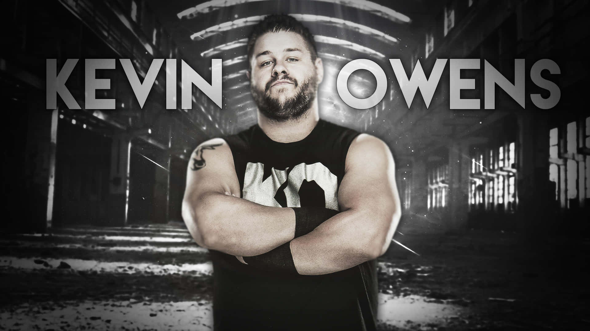 WWE 桌布 壁紙 — Kevin Owens 自信地交叉雙臂，站在一個粗糙、單色的工業走廊中，光線戲劇性。