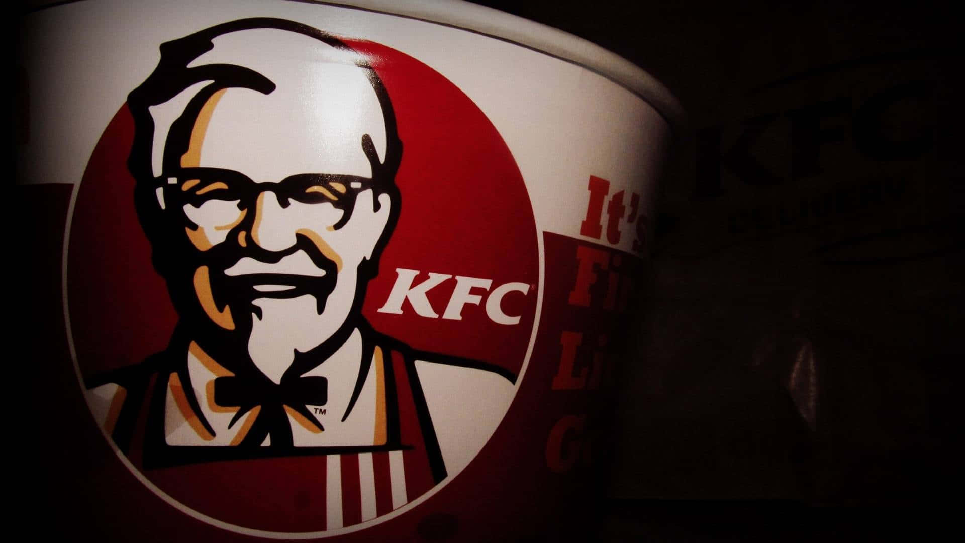 Kfc 桌布 壁紙 — KFC 桶的特寫，在戲劇性的低光照明下展示桑德斯上校的標誌性標誌。