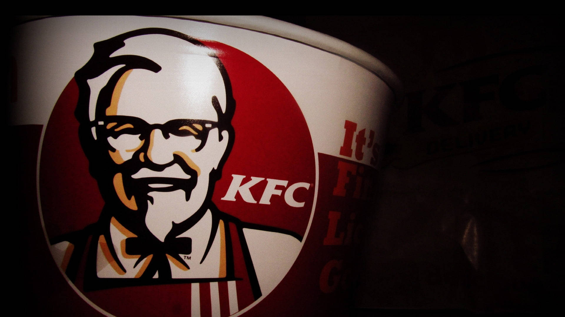 Kfc 桌布 壁紙 — KFC 桶的近距離特寫，在戲劇性的低光照明下展示桑德斯上校的標誌性標誌。