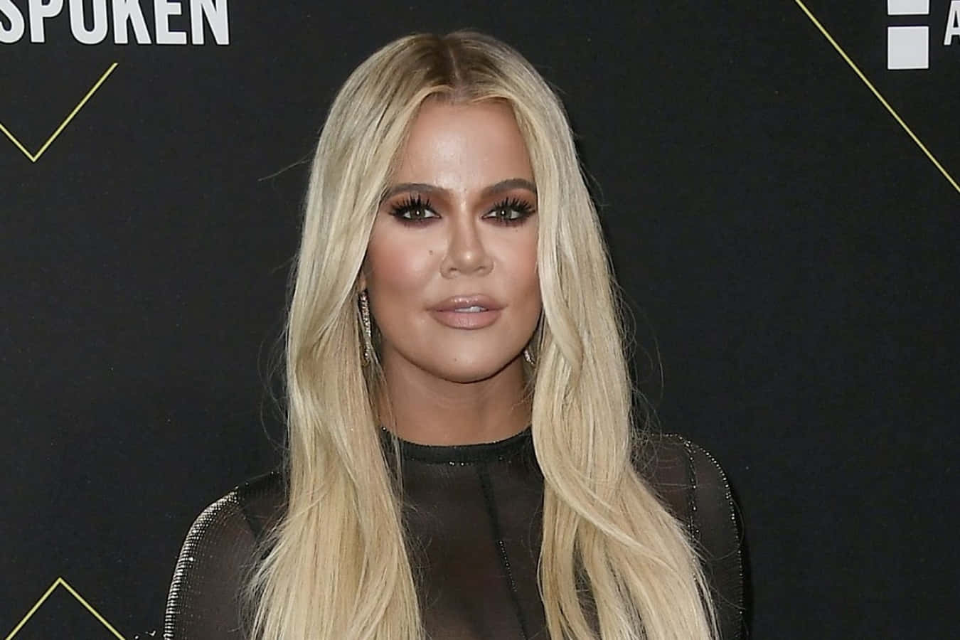 Khloe Kardashian 桌布 壁紙 — Khloé Kardashian 自信地擺姿勢，長長的金色頭髮和鮮豔的妝容，背景是黑色帶金色幾何線條。