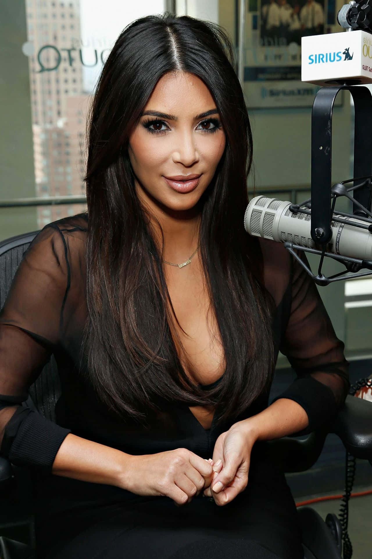 Kim Kardashian 桌布 壁紙 — Kim Kardashian 在攝影棚內從容就座，身穿黑色透視上衣，附近有麥克風。