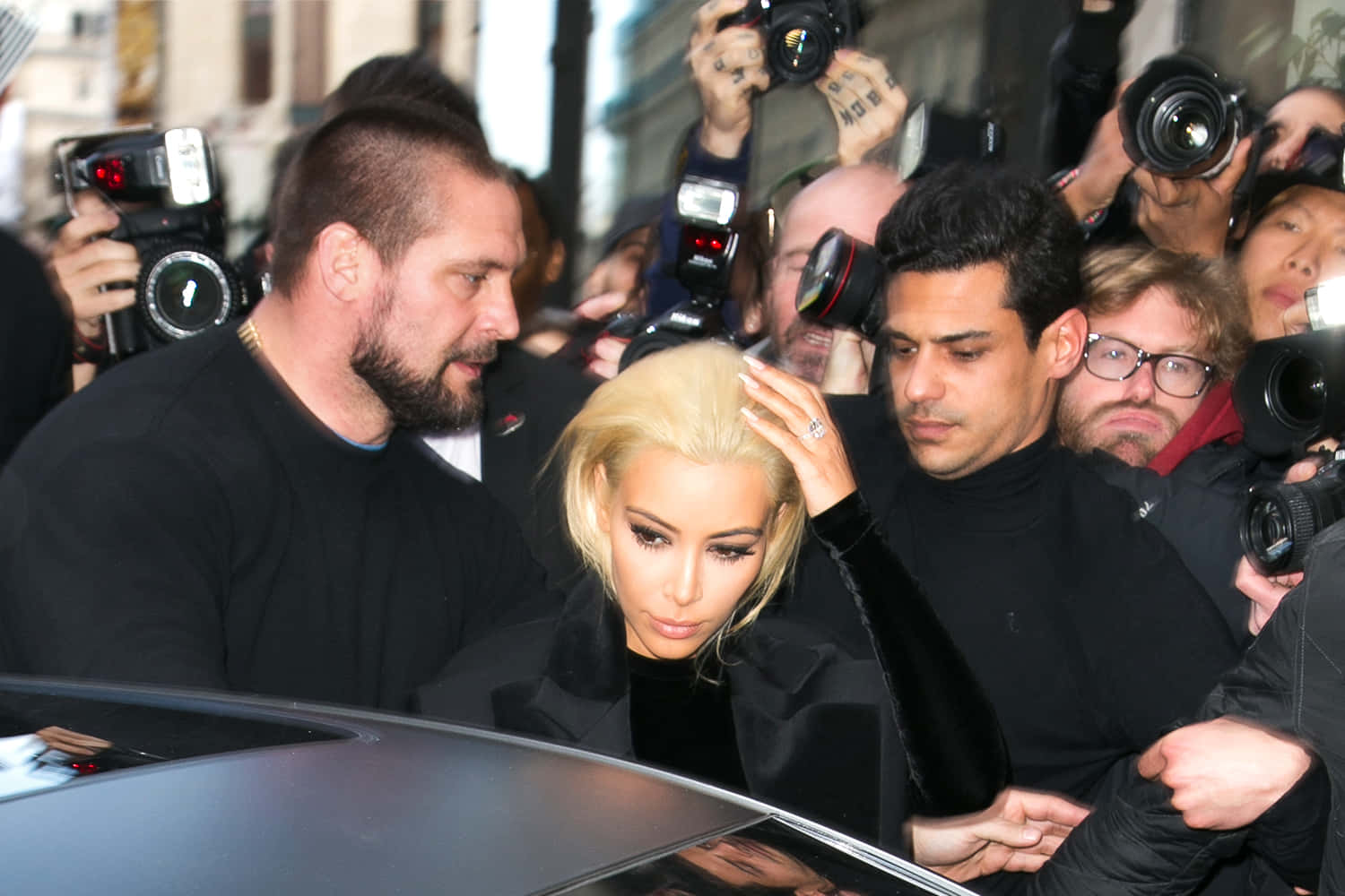 攝影師 桌布 壁紙 — Kim Kardashian 在保鏢護送下離開車輛，攝影師在擁擠的城市街道上閃光燈不斷。