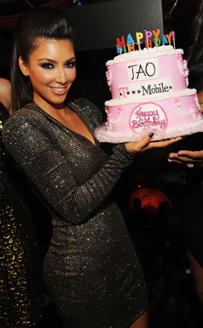 Birthday Party 桌布 壁紙 — Kim Kardashian 微笑著手持一個粉紅色兩層生日蛋糕，上面有T-Mobile品牌標誌和彩色蠟燭。