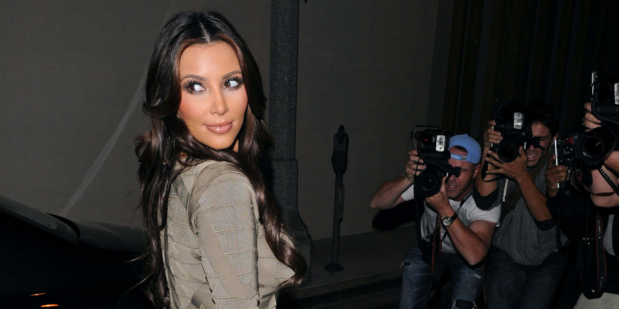 Paparazzi 桌布 壁紙 — Kim Kardashian 自信地微笑，回頭越過肩膀，攝影師在夜晚拍照。