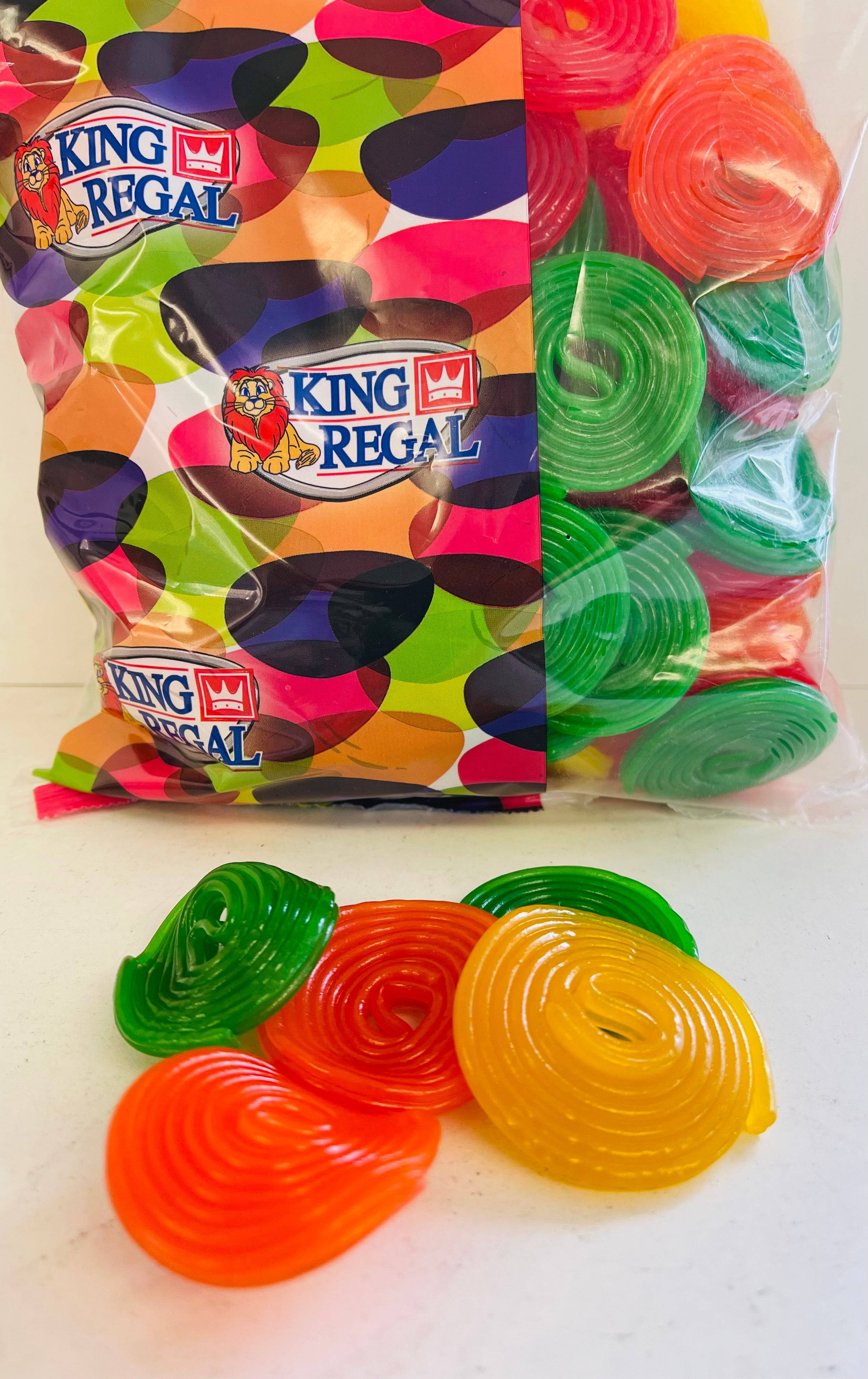 糖果 桌布 壁紙 — King Regal 軟糖的鮮豔漩渦從色彩繽紛的圖案包裝袋中灑落在白色表面上。