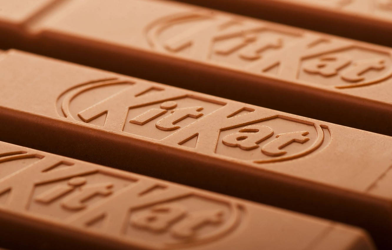 Chocolate 桌布 壁紙 — KitKat 巧克力棒的近距離特寫，展示壓花標誌，帶有溫暖的棕色色調和柔和光線。
