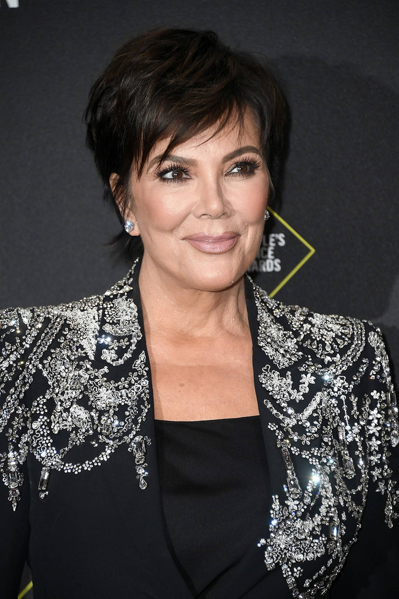 kris 桌布 壁紙 — Kris Jenner 在頒獎活動中穿著飾有閃亮銀色裝飾的黑色西裝外套，優雅地微笑。