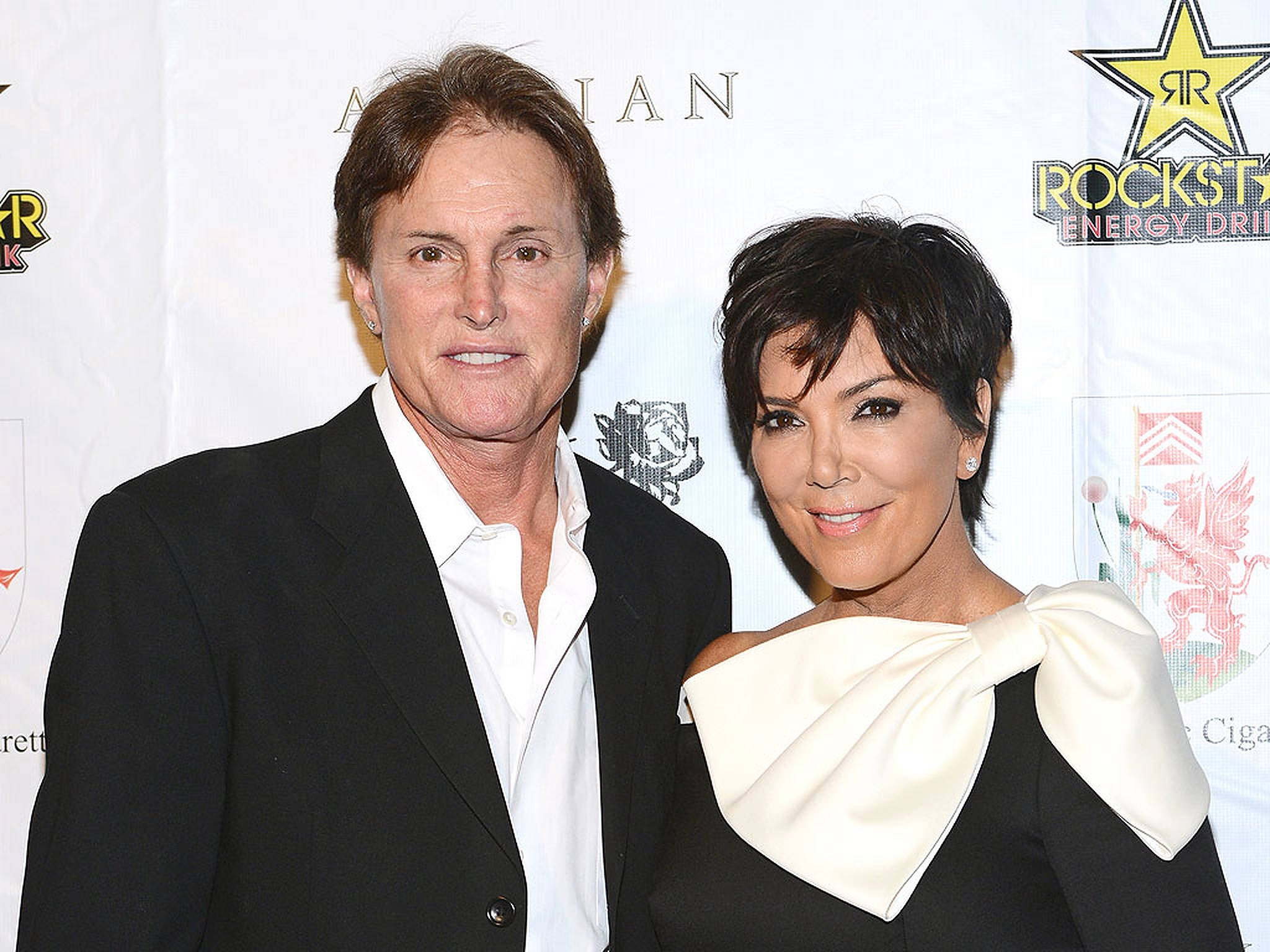kris 桌布 壁紙 — Kris Jenner 與丈夫在Rockstar Energy Drink活動中穿著正式服裝，在品牌背景前合影。