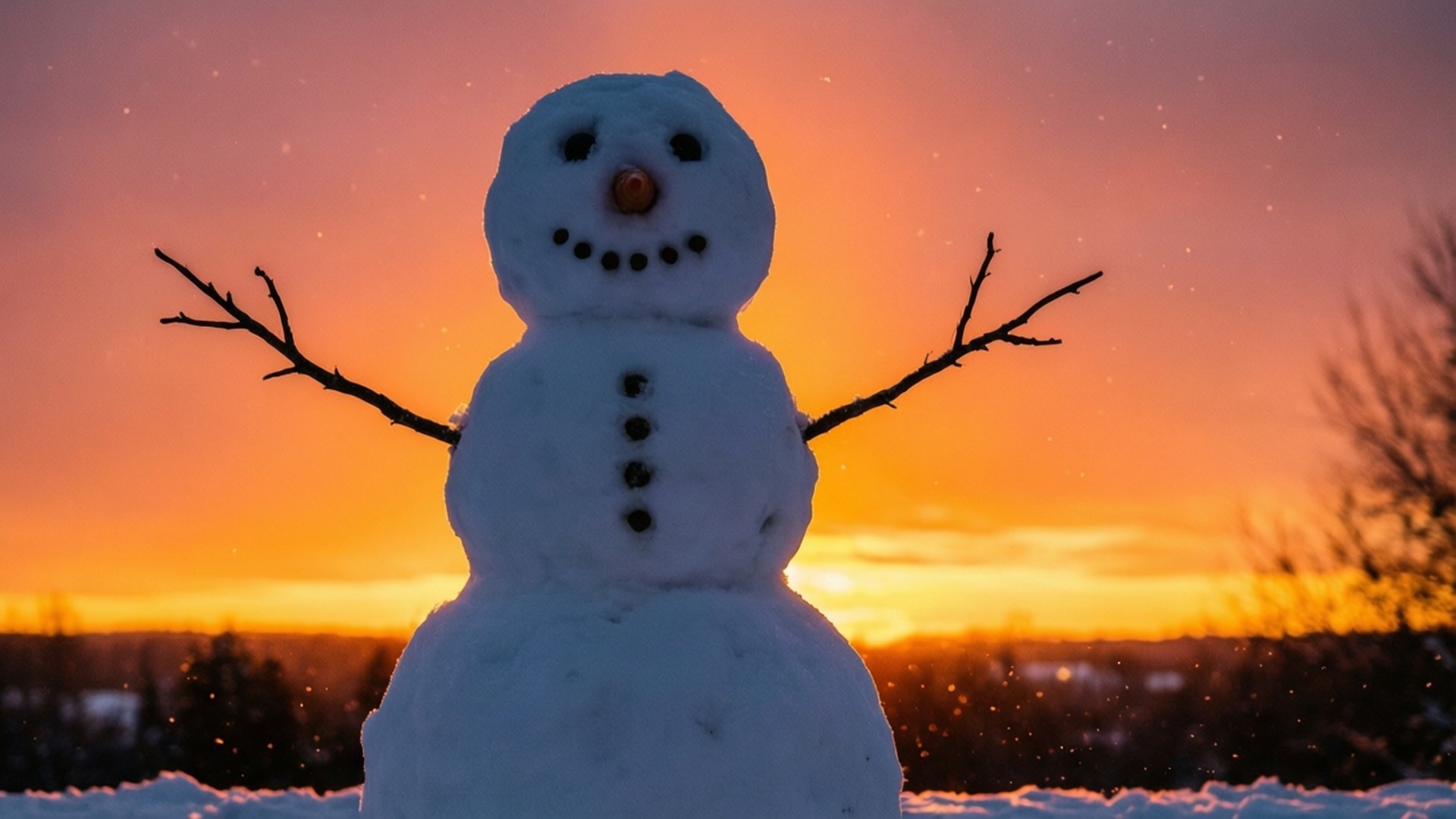 Snowman Silhouette Sunset 壁紙 — 一個快樂的雪人，有樹枝手臂和煤鈕扣，站在充滿活力的橙色和粉紅色日落天空前。