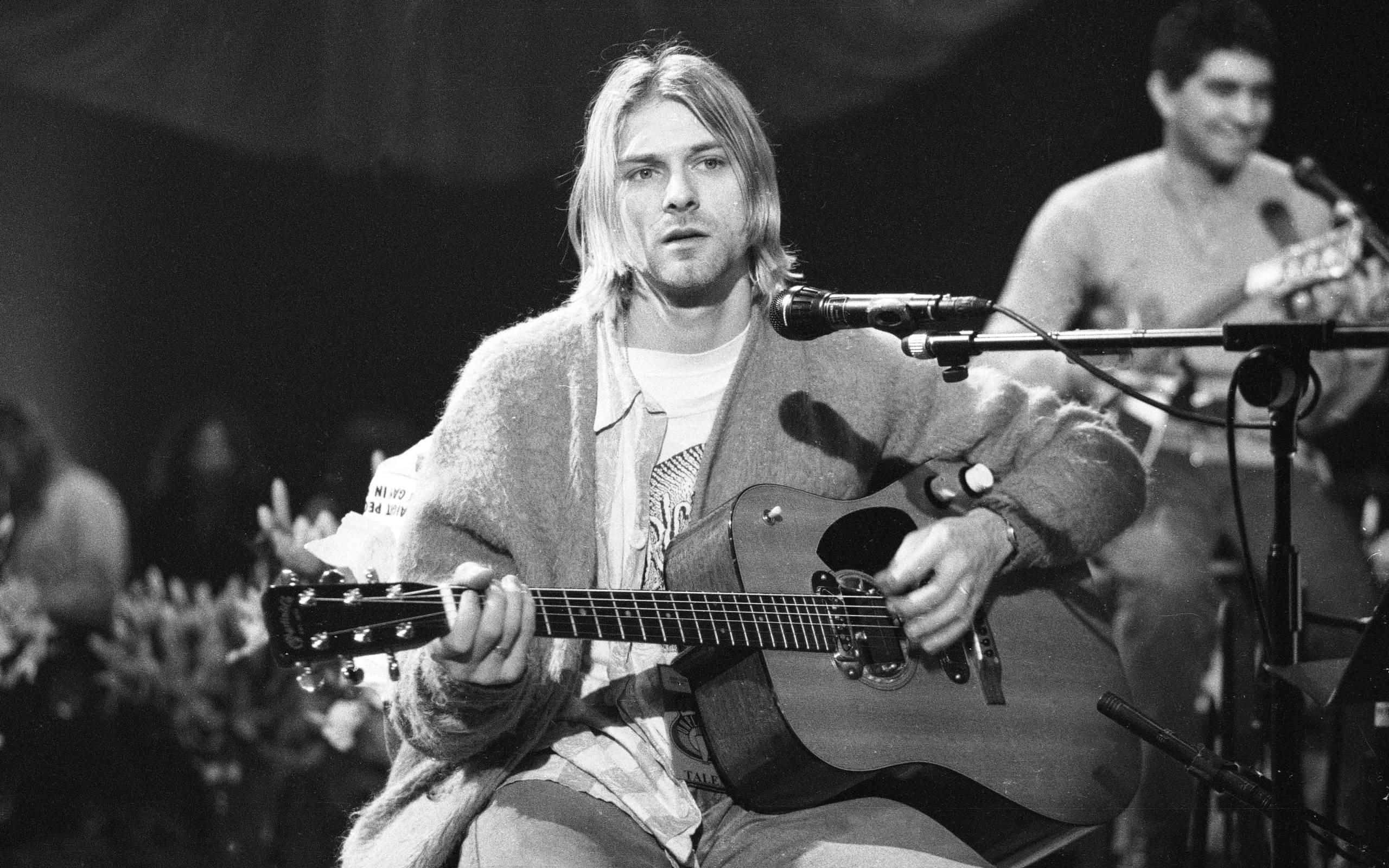 nirvana 桌布 壁紙 — Kurt Cobain 在舞台上彈奏木吉他，黑白影像，在舞台燈光下展現高度專注。