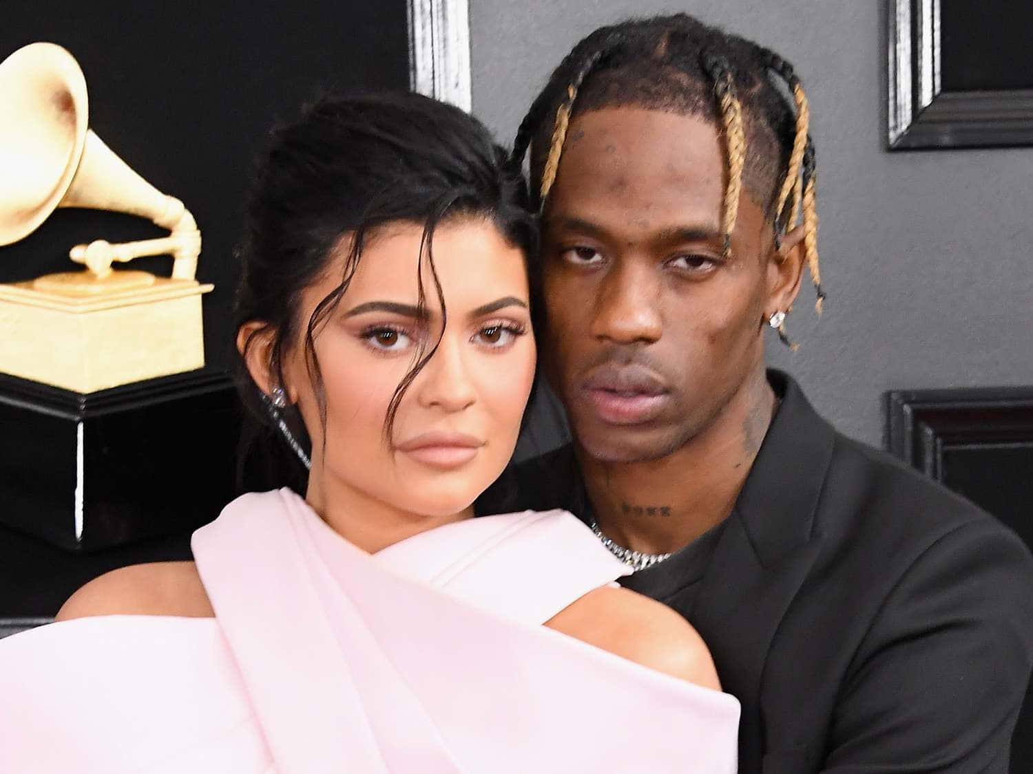 崔維斯·史考特 桌布 壁紙 — Kylie Jenner 和 Travis Scott 在葛萊美獎活動中緊密擺姿勢，背景有金色獎盃。