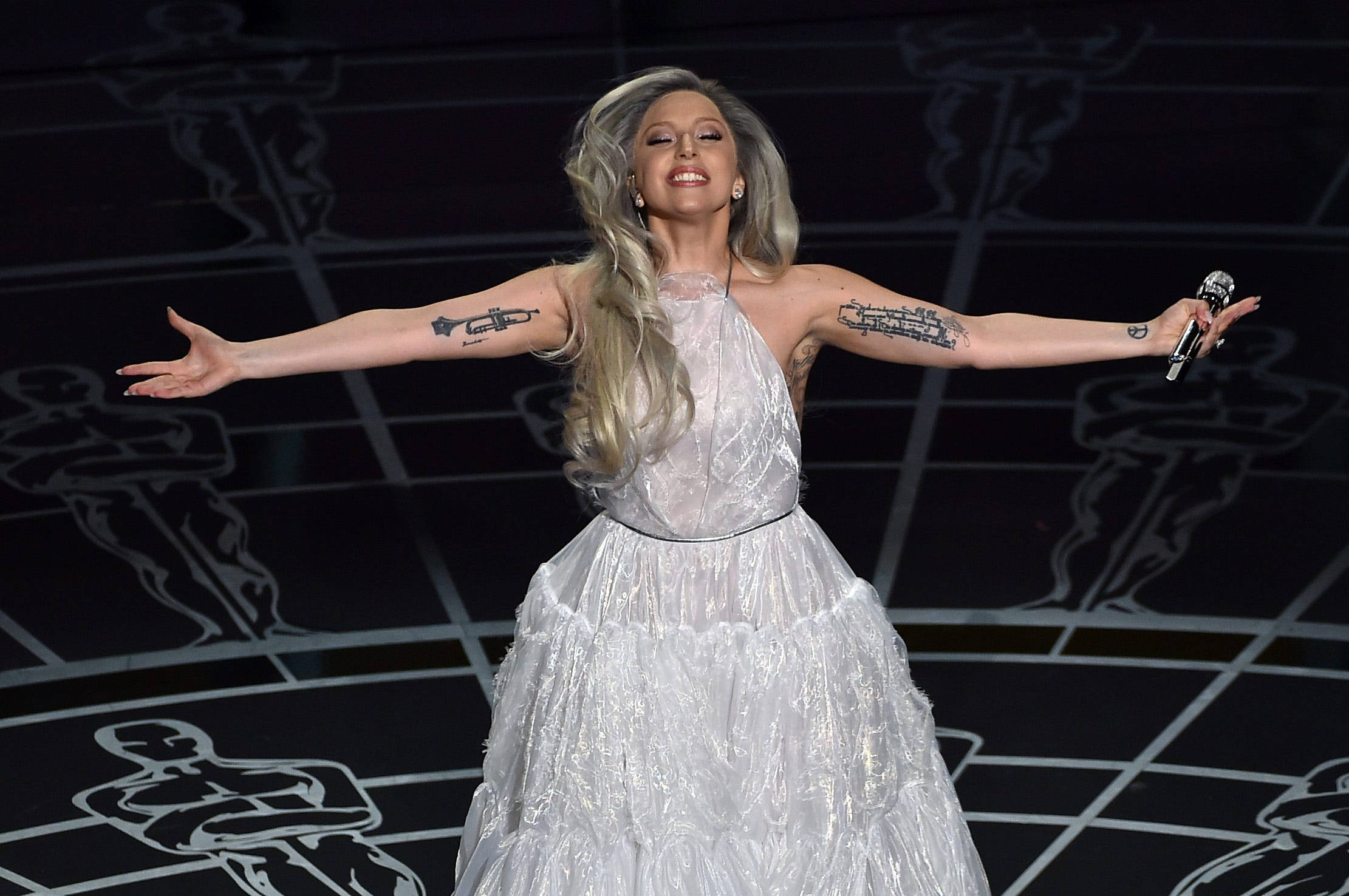 lady 桌布 壁紙 — Lady Gaga 在舞台上表演，身穿閃閃發光的白色長袍，雙臂伸展，手持麥克風。