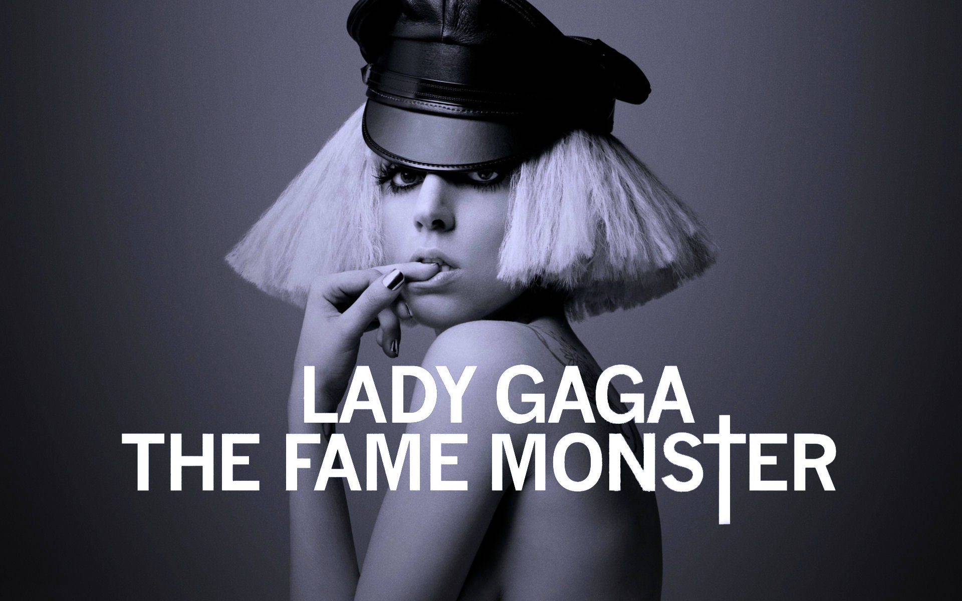 lady 桌布 壁紙 — Lady Gaga 戴著黑色皮帽和白色波波頭假髮，在深灰色背景上將手指放在嘴唇上，並帶有專輯文字。