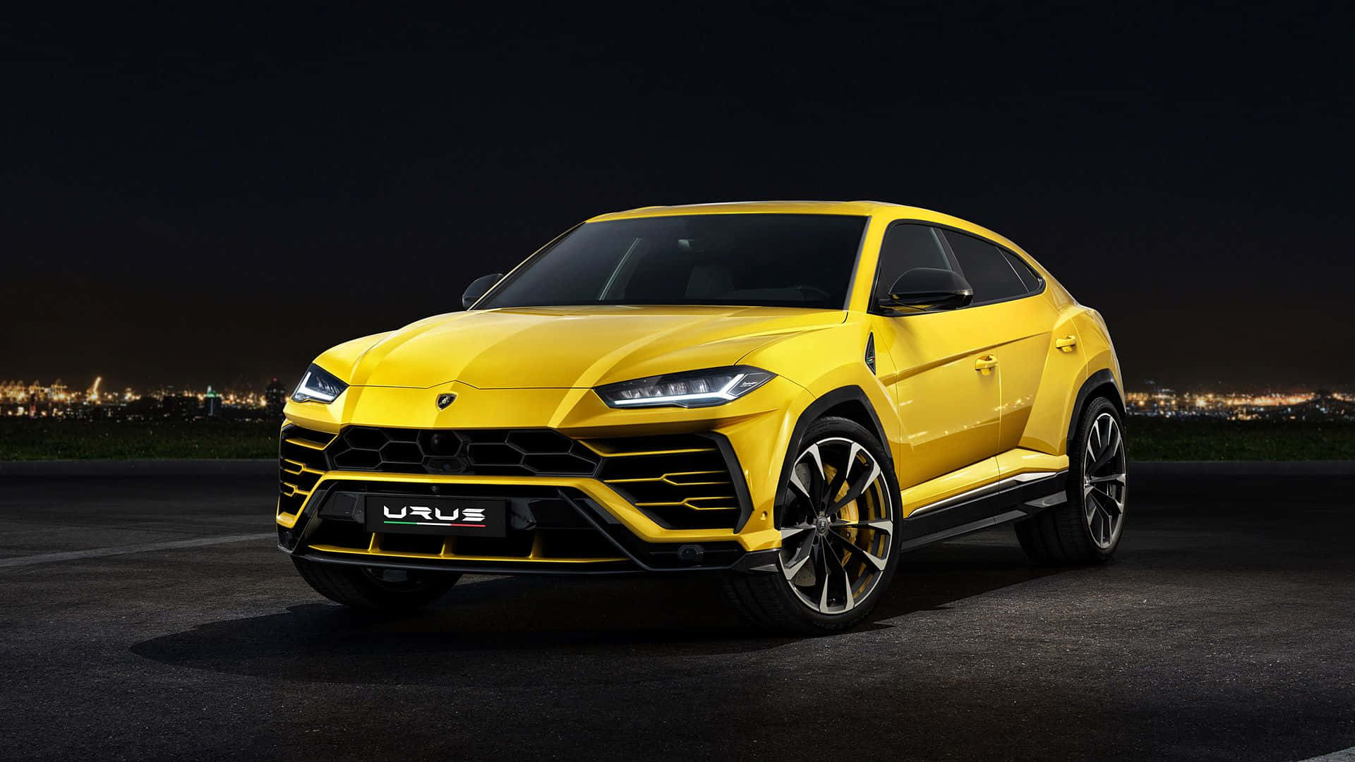 Lamborghini Urus 桌布 壁紙 — 一輛鮮黃色的藍寶堅尼 Urus SUV 在夜燈下閃耀，背景是發光的城市天際線。