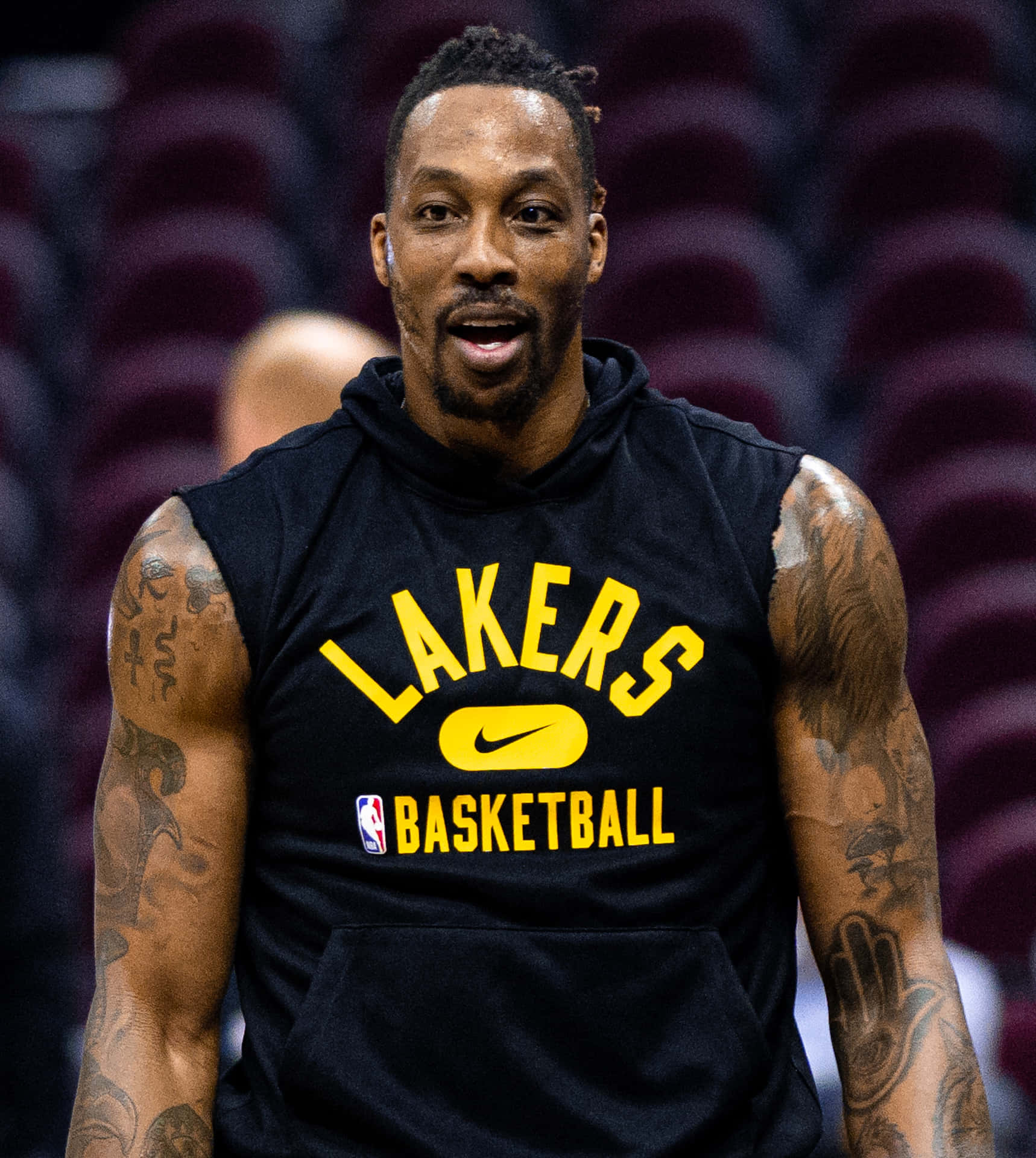  壁紙 — 一名籃球運動員身穿黑色Lakers連帽衫，帶有黃色字樣，站在身後有酒紅色座位的場館中。