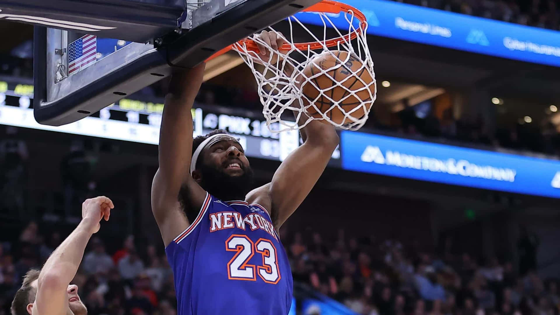 身穿藍色球衣的籃球運動員在比賽中灌籃，背景有觀眾。 — NBA 壁紙