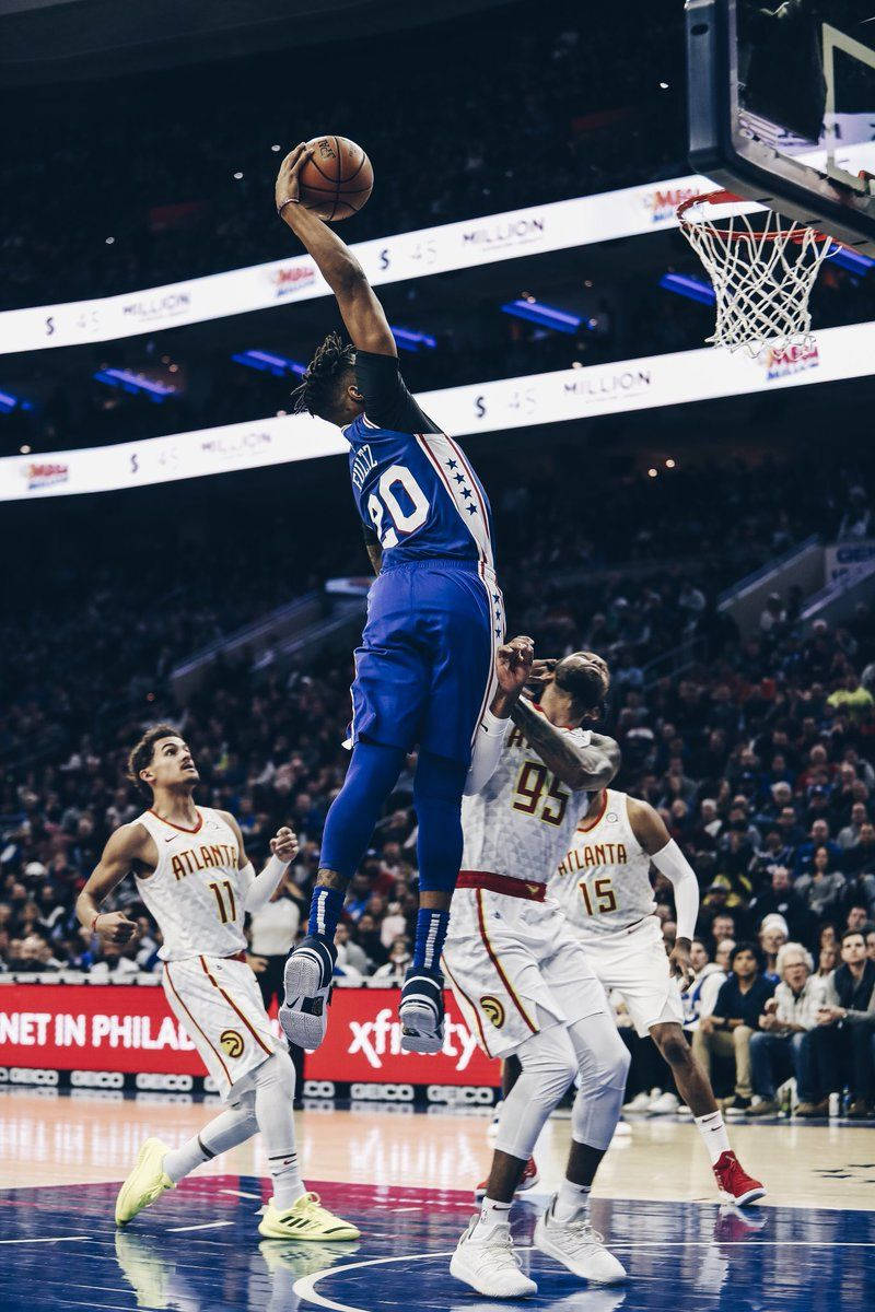 籃球運動員在擠滿觀眾的場館中空中灌籃越過防守球員。 — NBA 壁紙
