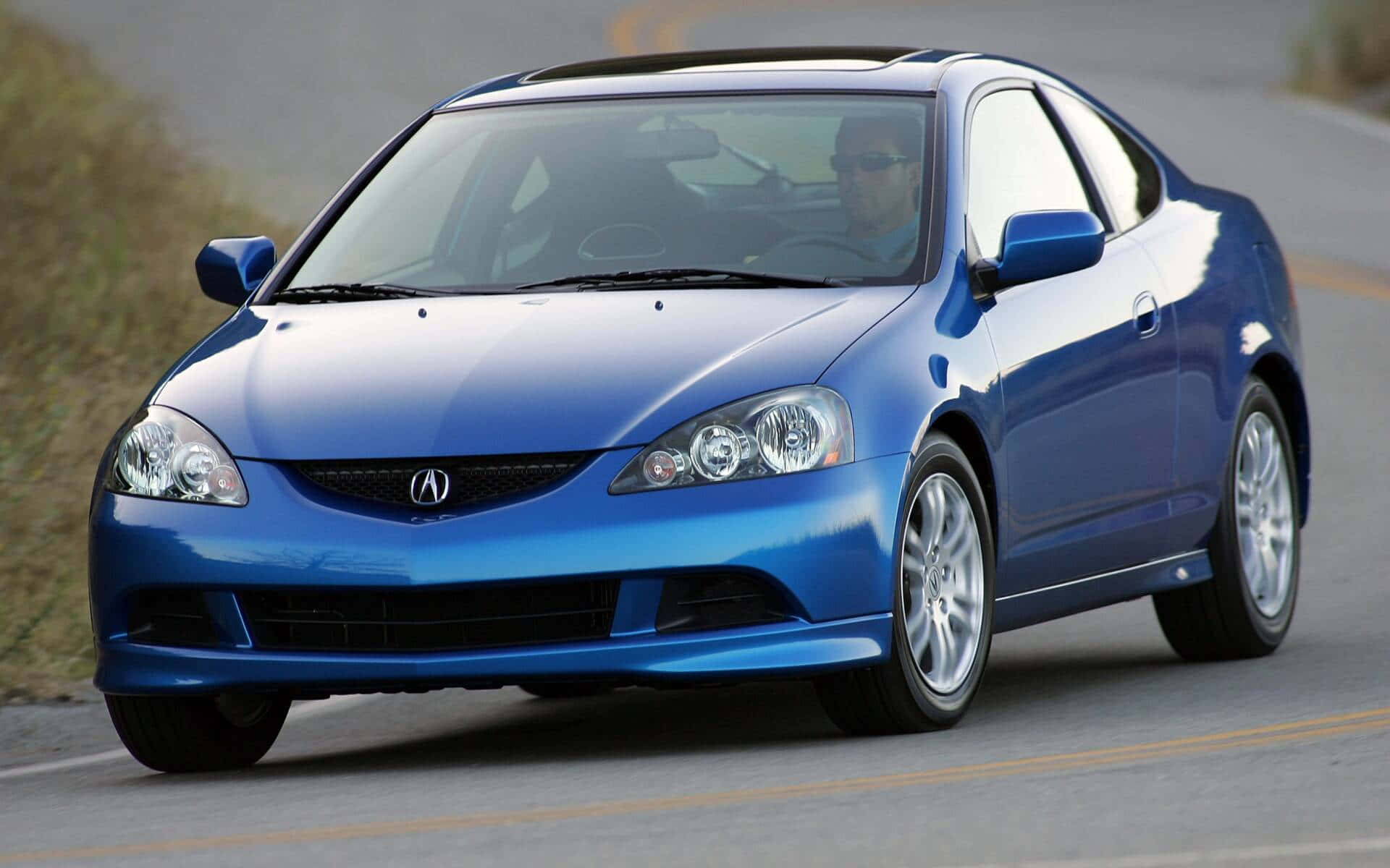 Acura Rsx 桌布 壁紙 — 一輛充滿活力的藍色Acura RSX雙門跑車在陽光明媚的道路上行駛，透過擋風玻璃可以看到駕駛員。