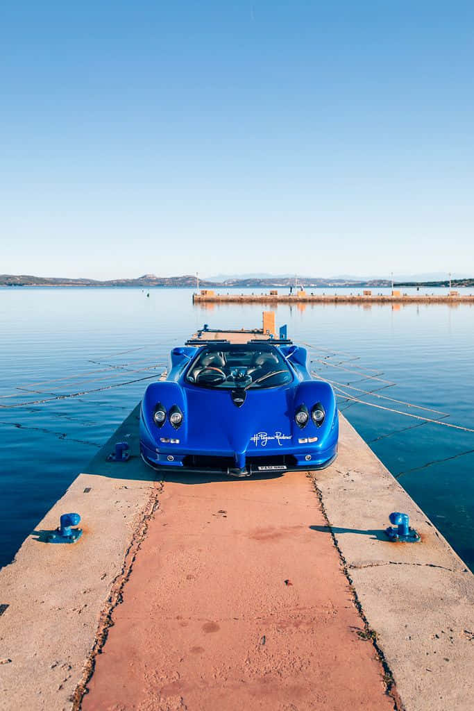 Pagani Zonda C12 Roadster 桌布 壁紙 — 一輛充滿活力的藍色Pagani跑車停泊在一個風化了的碼頭上，旁邊是平靜的藍綠色海水，天空清澈湛藍。
