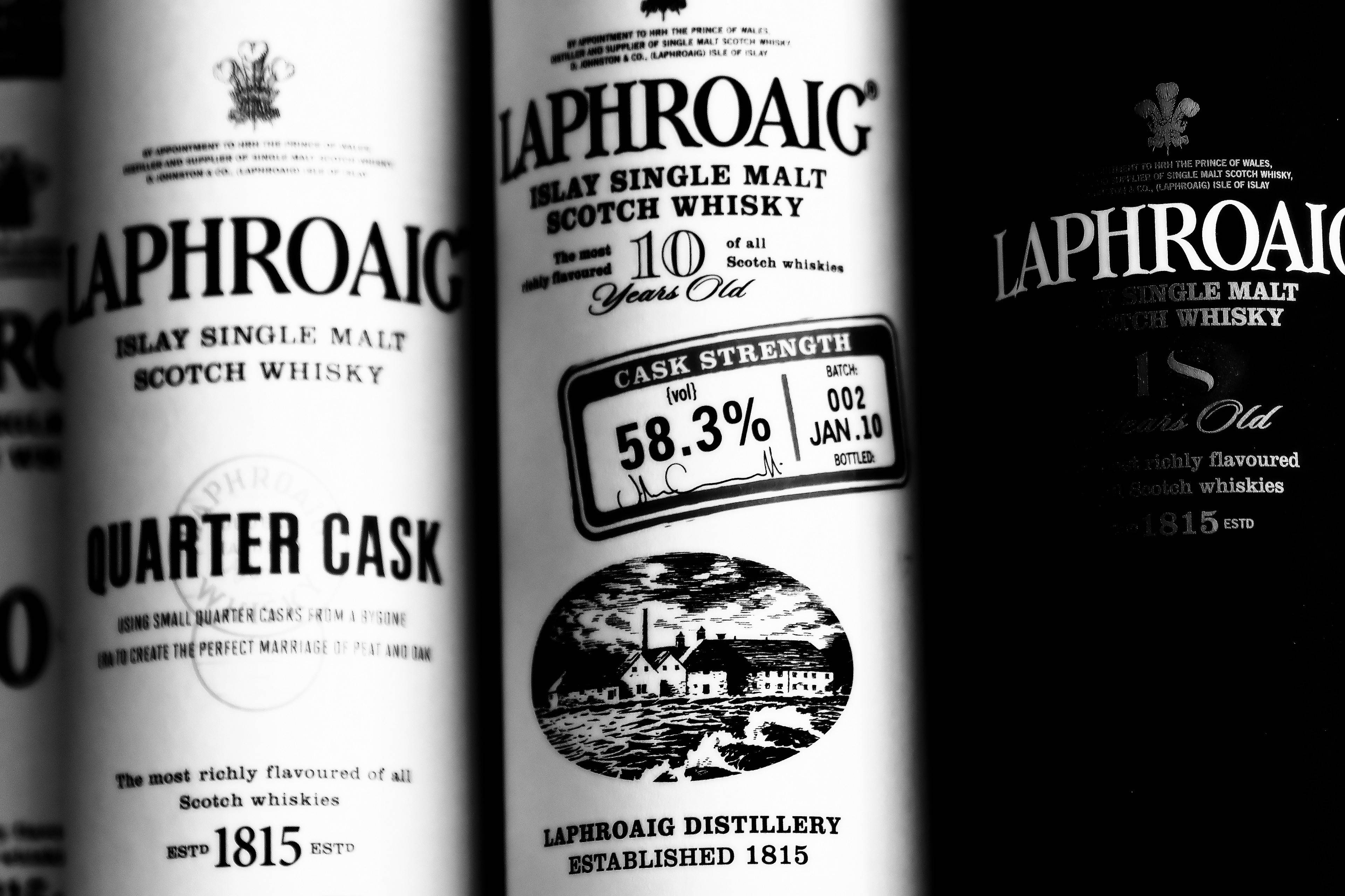 手機 桌布 壁紙 — Laphroaig 威士忌酒瓶特寫，帶有粗體文字和復古蒸餾廠插圖，高對比度黑白。