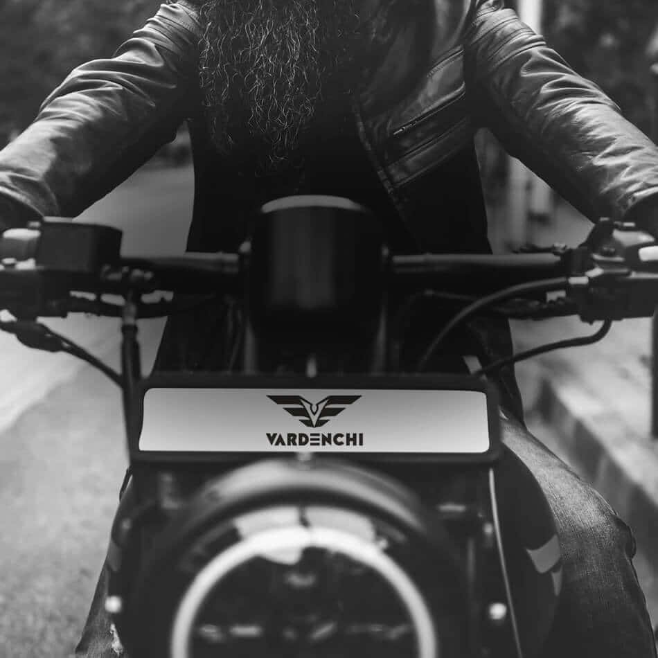 Vardenchi 桌布 壁紙 — 一位留鬍子的騎士穿著皮夾克，在充滿氣氛的黑白街頭照片中握著VARDENCHI摩托車的把手。