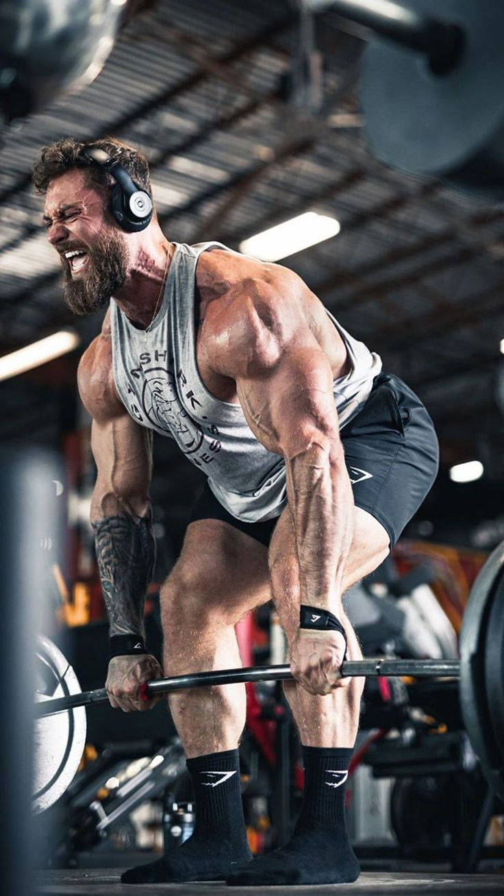 留鬍子男人在健身房舉槓鈴，表情激烈 — Chris Bumstead 壁紙