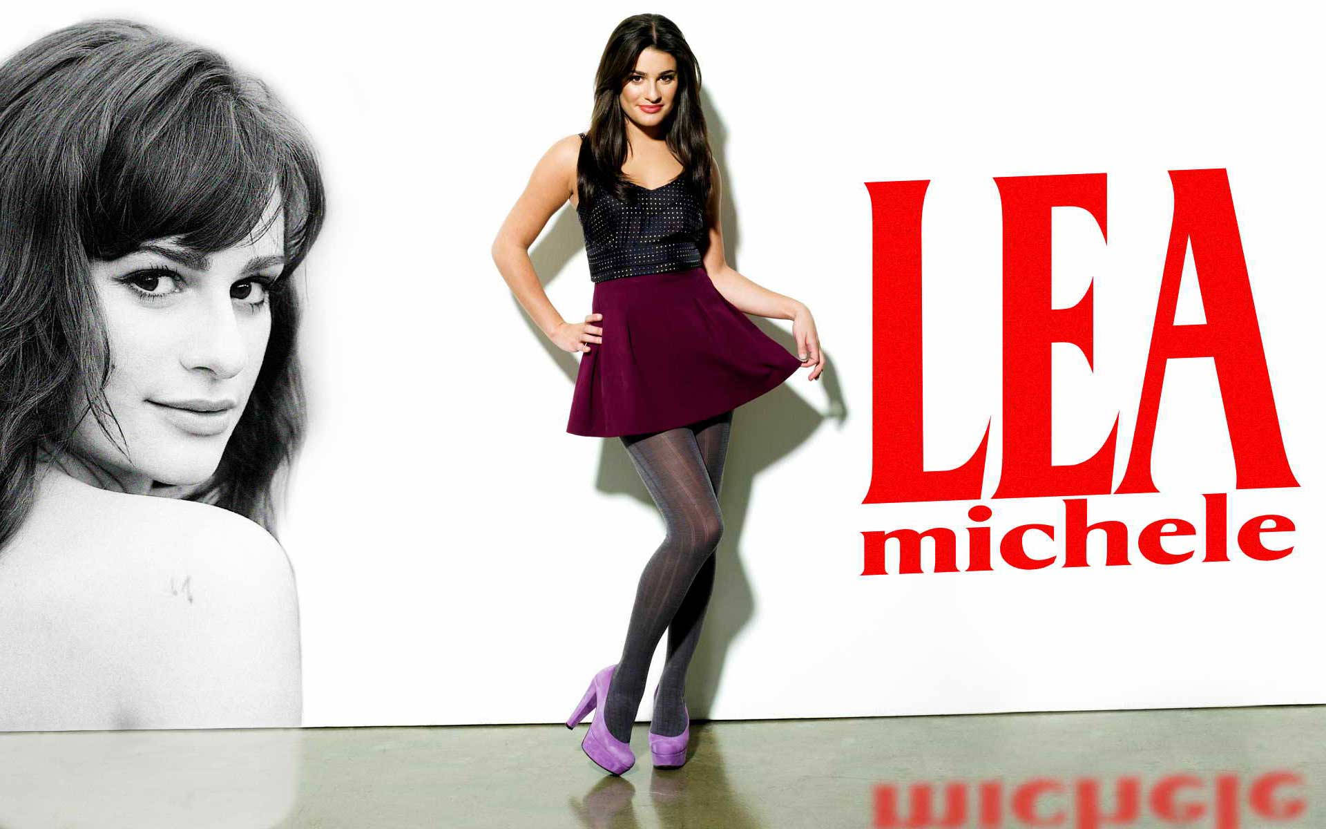 Lea Michele 桌布 壁紙 — Lea Michele 自信地擺姿勢，身穿黑色上衣和紫色裙子，背景為白色，她的名字以粗體紅色字母呈現。