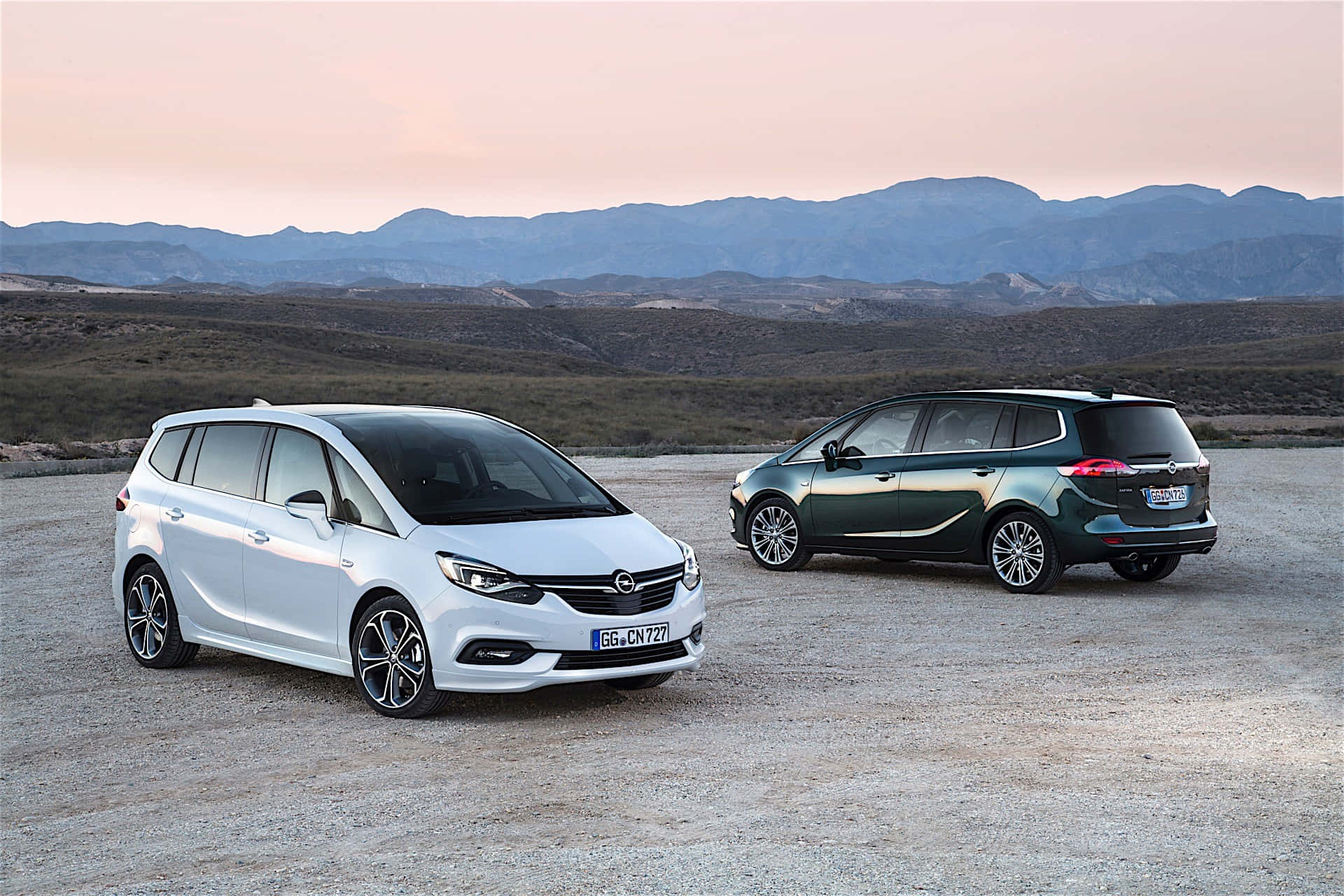 Opel Zafira 桌布 壁紙 — 兩輛現代歐寶Mokka客貨車停在碎石上，遠處山巒在柔和粉紅與橙色日落天空下。