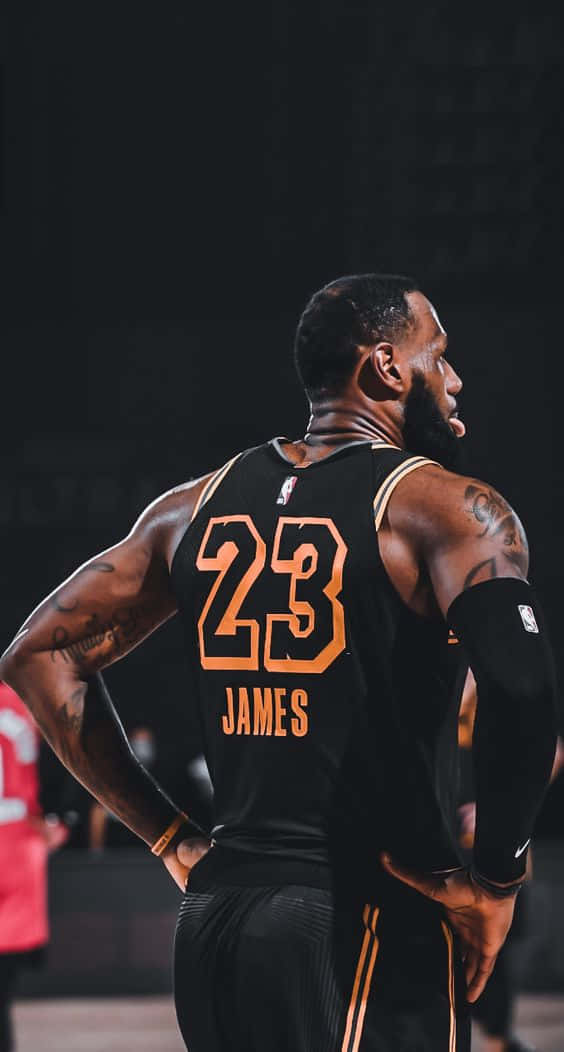 勒布朗詹姆斯身穿黑色和橙色球衣，雙手叉腰站立。 — King Lebron James 壁紙