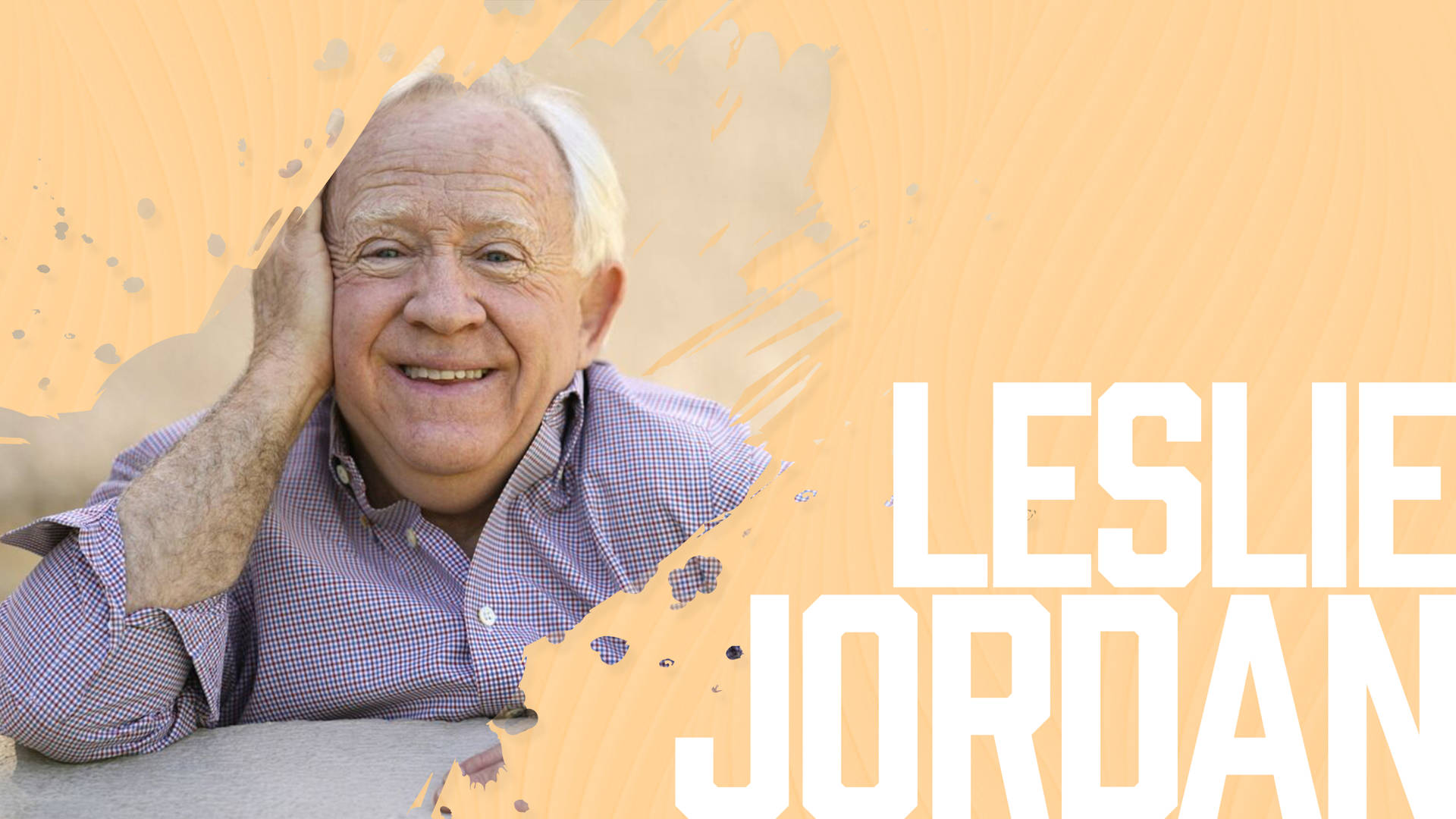Leslie Jordan 在橙色紋理背景前將手放在臉頰上微笑。 — Jordan Logo 壁紙