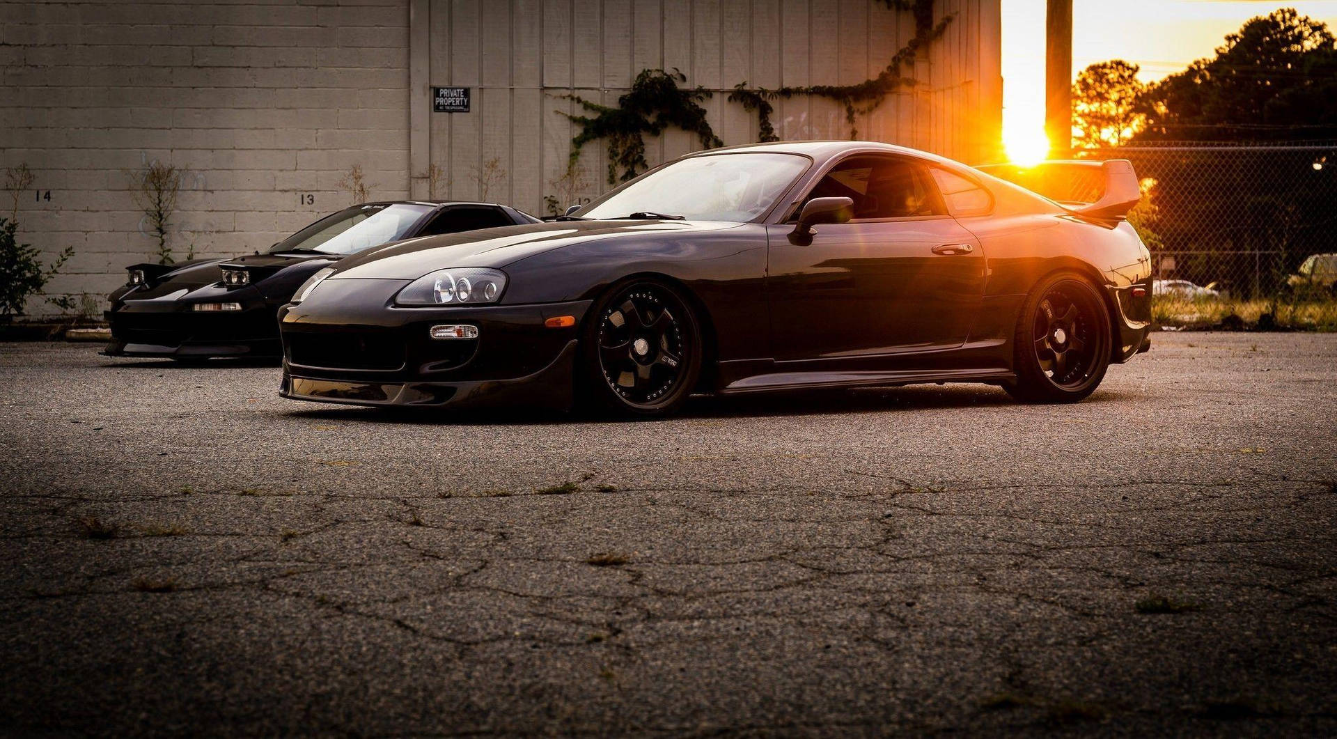 日落時分，兩輛黑色跑車停泊在倉庫前。 — Toyota Supra 壁紙