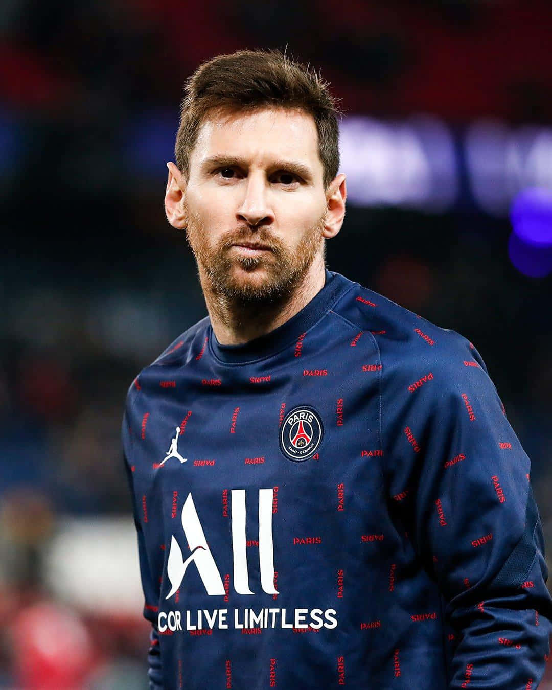 Messi 2022 桌布 壁紙 — 利昂內爾·梅西身穿巴黎聖日耳曼訓練上衣，在球場燈光下專注地凝視鏡頭。