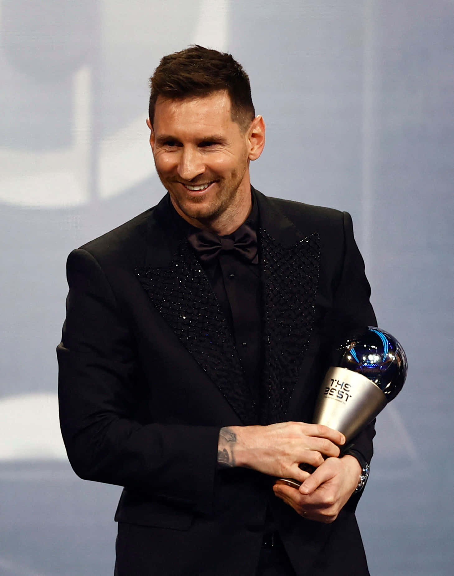  壁紙 — 利昂內爾·梅西身穿黑色亮片西裝，在舞台上自豪地捧著The Best FIFA Football Award。