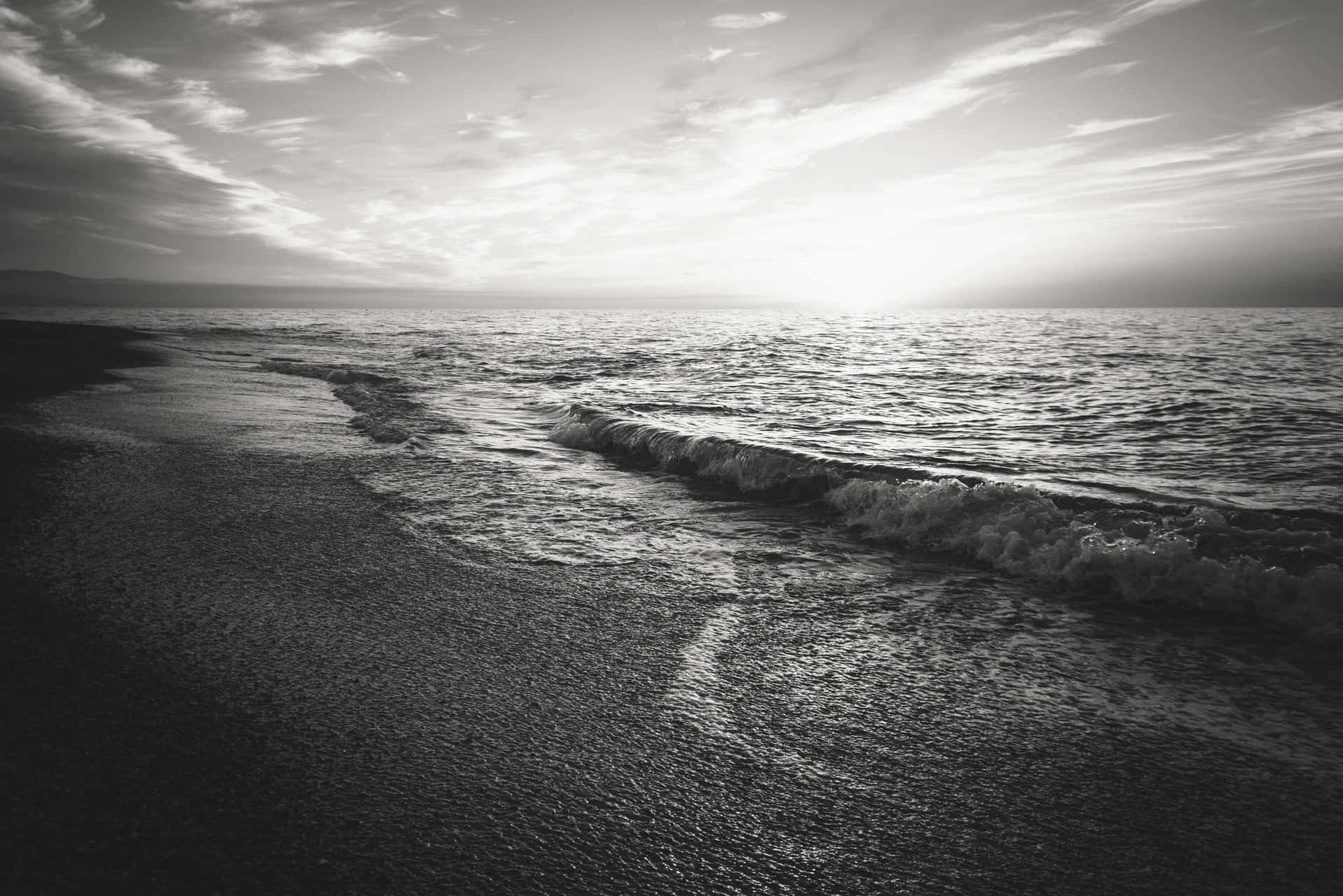  壁紙 — 黎明時分，在柔和的多雲天空下，單色波浪輕輕拍打沙灘。