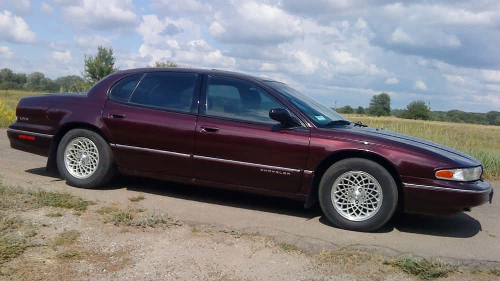Chrysler Lhs 桌布 壁紙 — 一輛栗色Chrysler LHS轎車停泊在碎石路上，旁邊是草地，天空多雲。