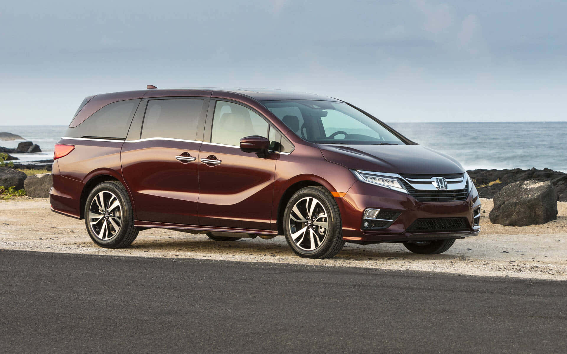 Honda Odyssey 桌布 壁紙 — 一輛栗色本田Odyssey小型貨車停泊在沿海道路上，背景是海洋和岩石，天空多雲。