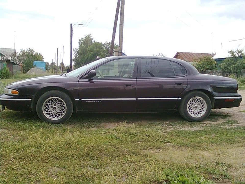 Chrysler Lhs 桌布 壁紙 — 一輛栗色雪佛蘭轎車停在草地上，背景有電線桿和房屋，天空多雲。