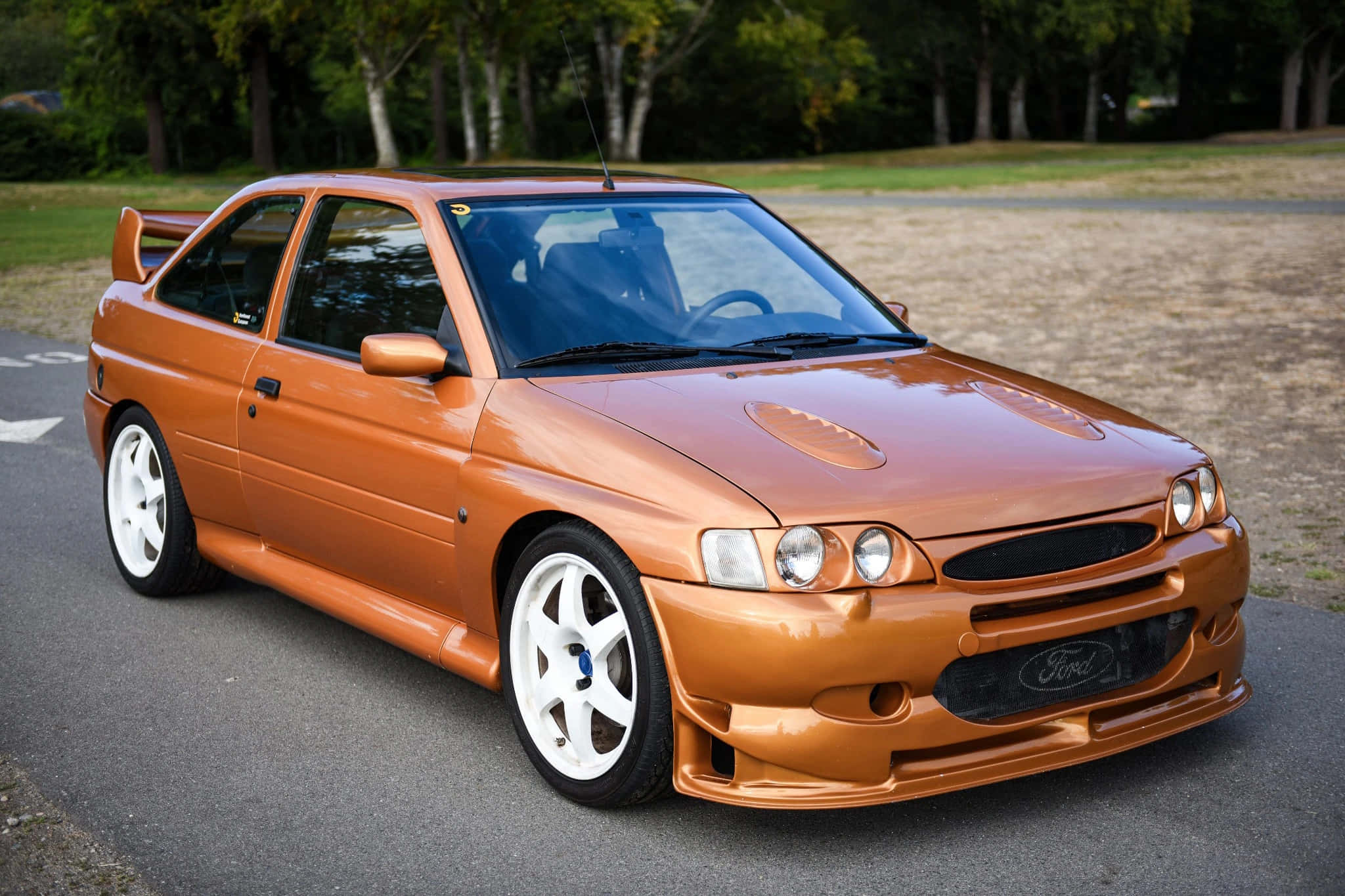 Ford Escort 桌布 壁紙 — 一輛亮橙色的福特Escort RS Cosworth跑車停在瀝青路上，背景有樹木。