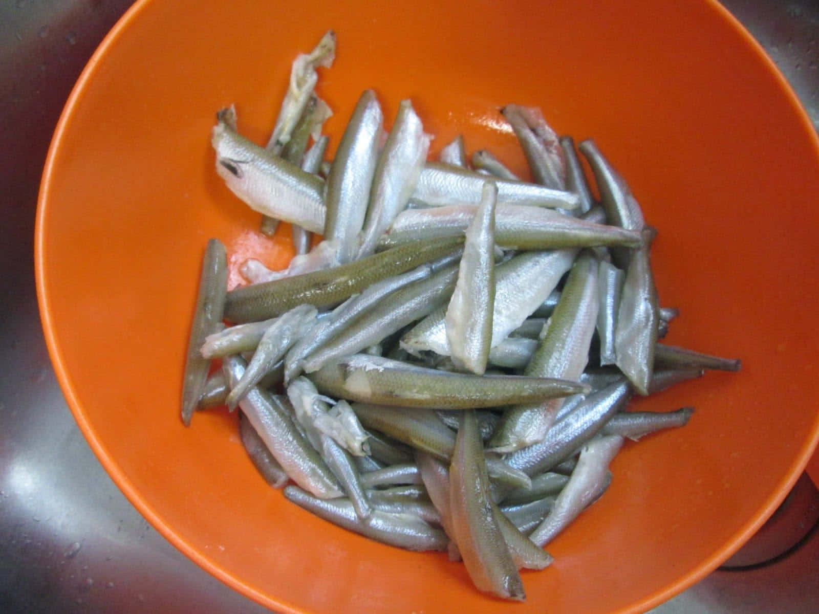  壁紙 — 一個亮橙色的碗裝滿了銀色小魚，放在不鏽鋼水槽中。