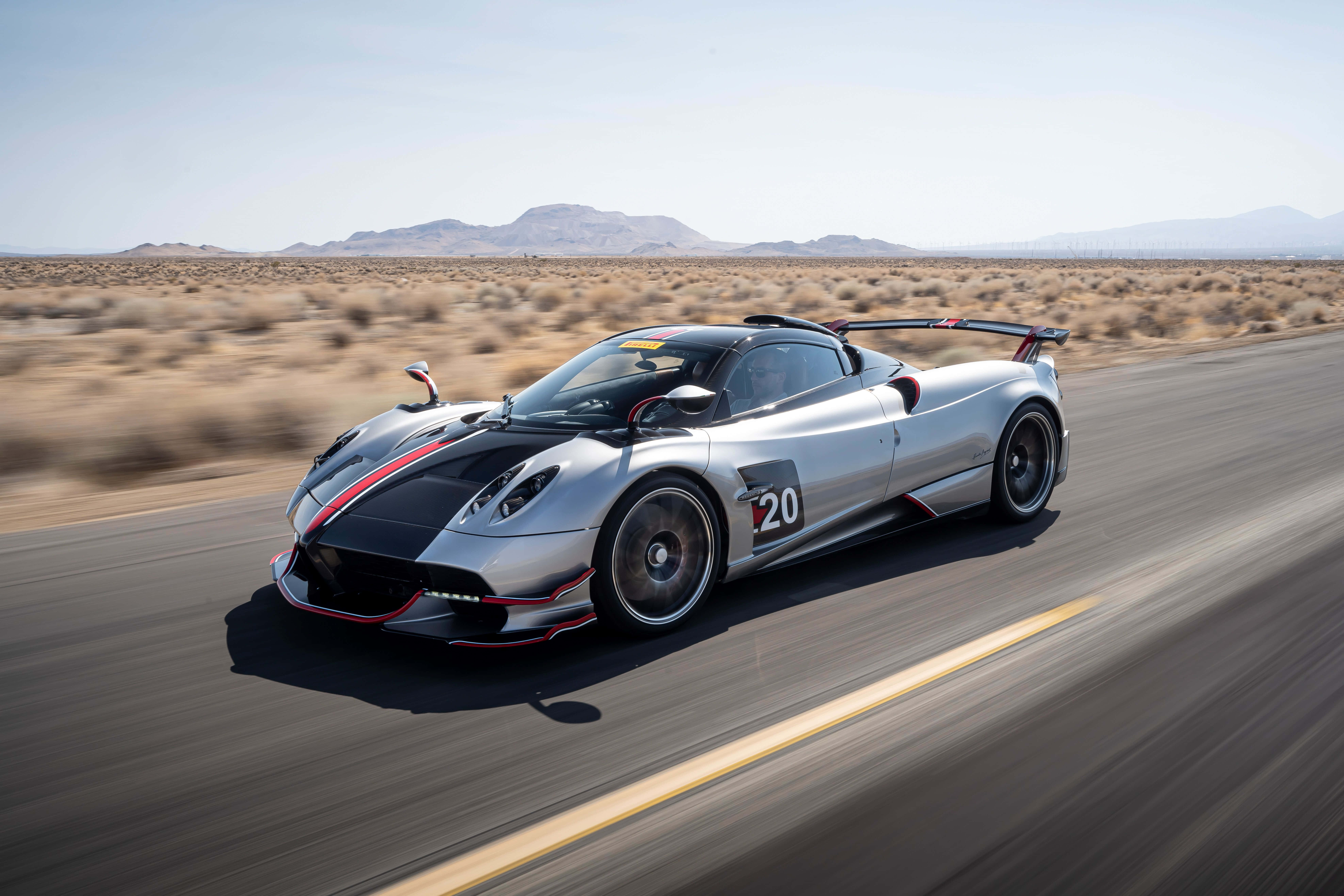 Pagani Huayra Roadster Bc 桌布 壁紙 — 一輛帶有紅色點綴的銀色帕加尼超跑在晴朗藍天下於沙漠公路上飛馳。