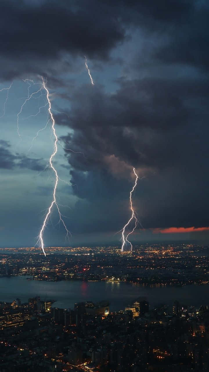 Lightning iPhone 桌布 壁紙 — 兩道巨大的閃電照亮了暴風雨的夜空，下方是燈火輝煌的廣闊城市景觀。