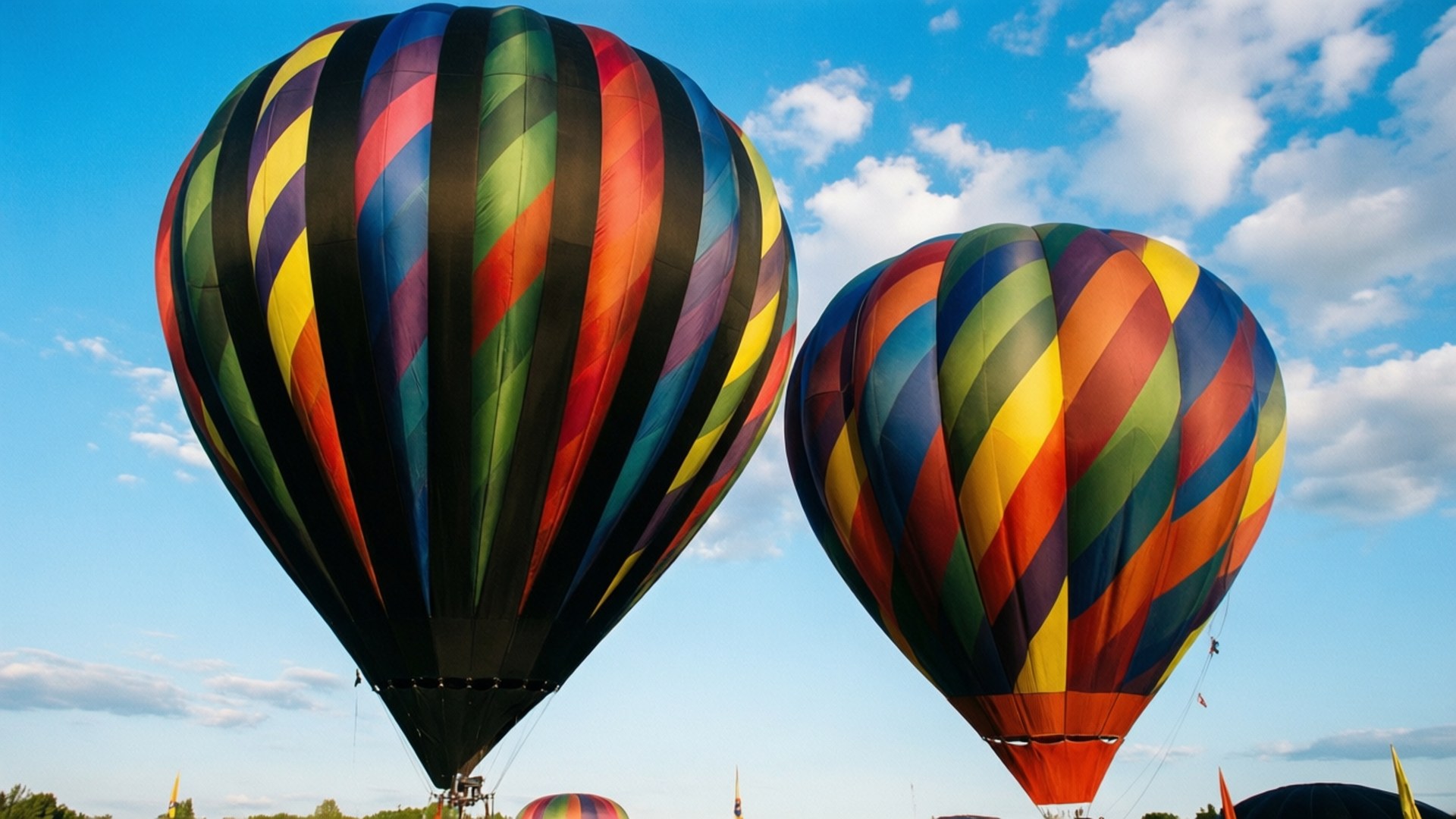 Balloon Festival Stripes 壁紙 — 兩個色彩鮮豔的彩虹條紋熱氣球在點綴著蓬鬆白雲的明亮藍天中飄浮。