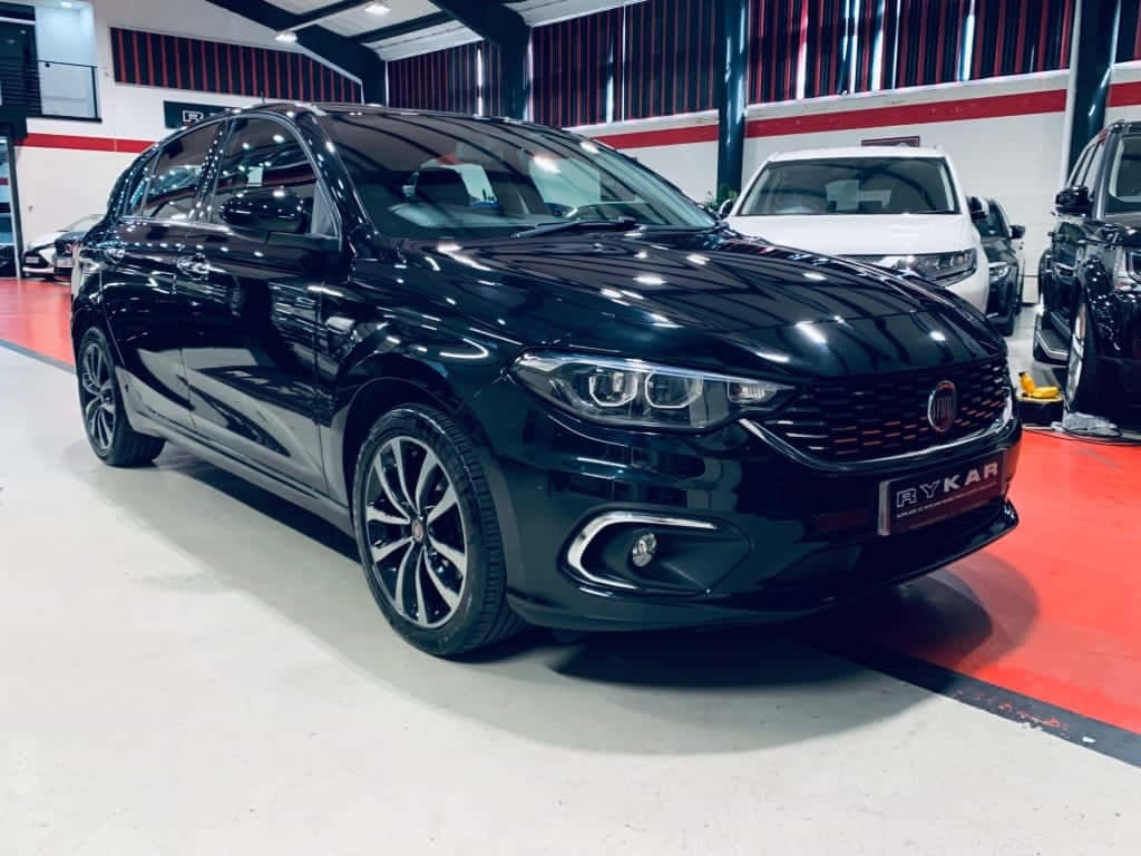 Fiat Tipo 桌布 壁紙 — 一輛光澤黑色Fiat Tipo掀背車在現代汽車展廳的明亮燈光下閃閃發光，帶有紅色點綴。